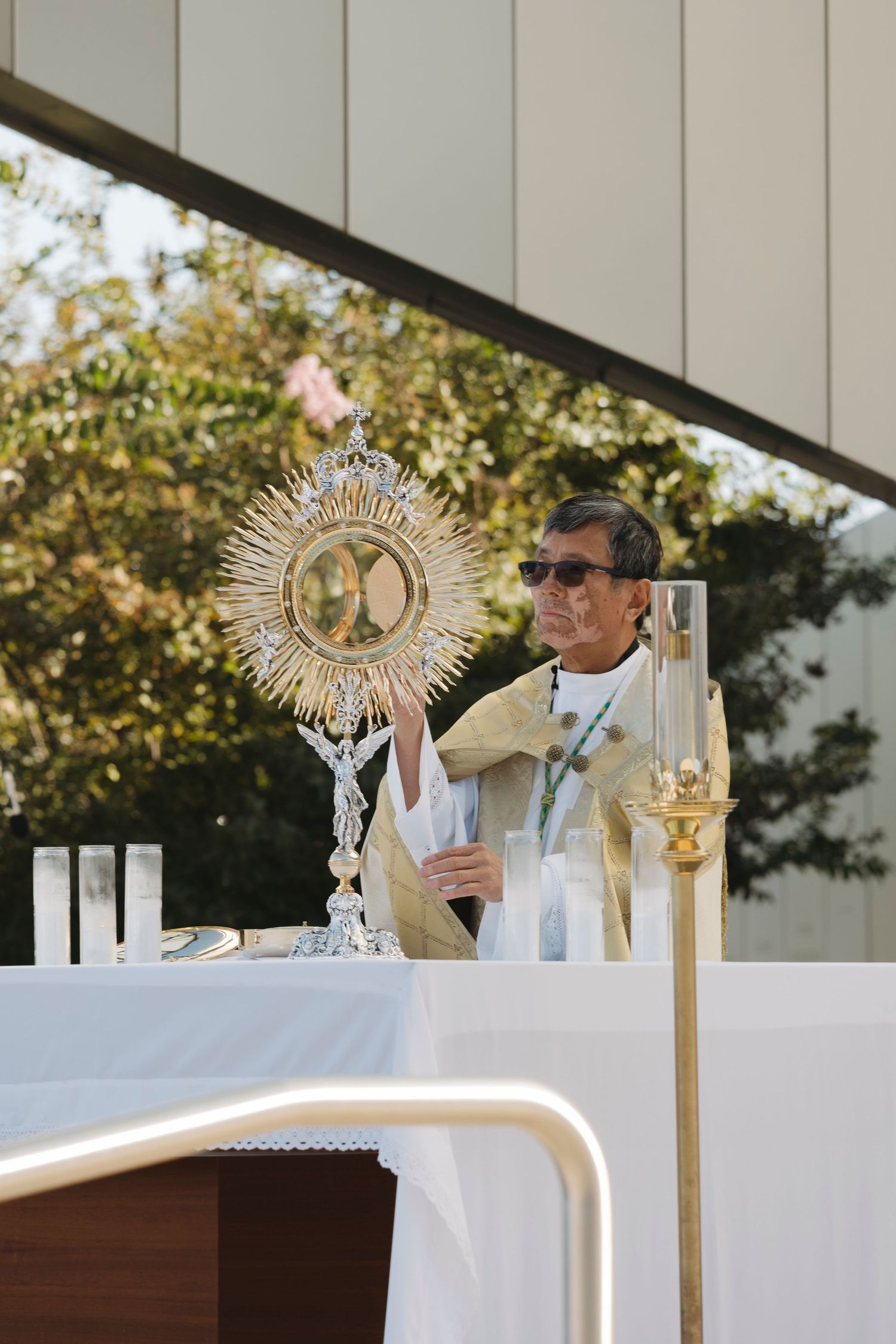 A priest conducts Eucharistic adoration with a golden monstrance on an outdoor altar.