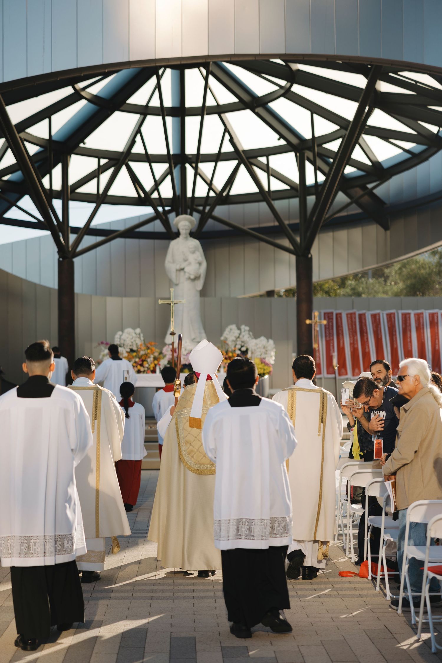Clergy members in traditional vestments gather under a modern architectural canopy.