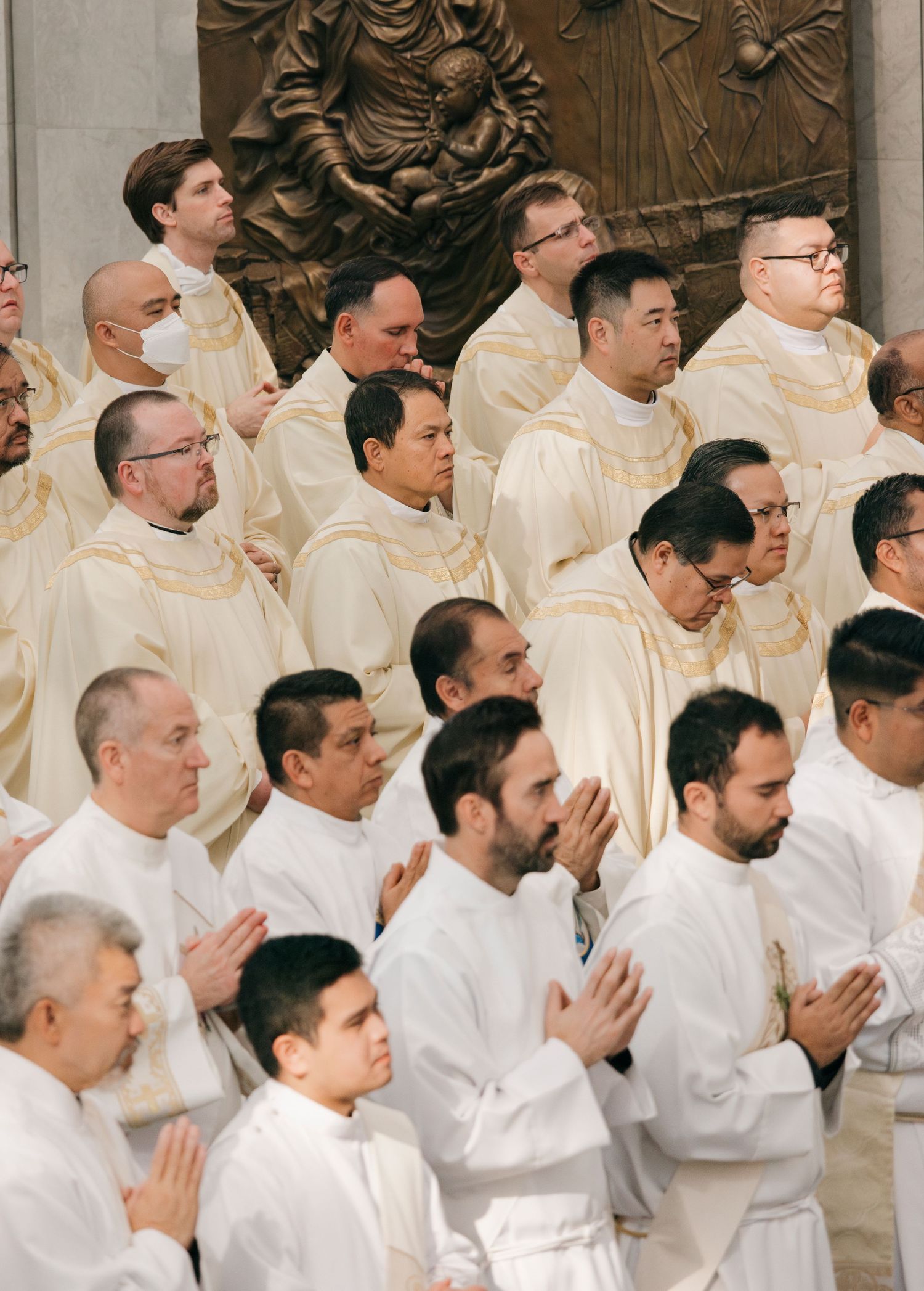 Row of priests in white robes praying during religious ceremony.