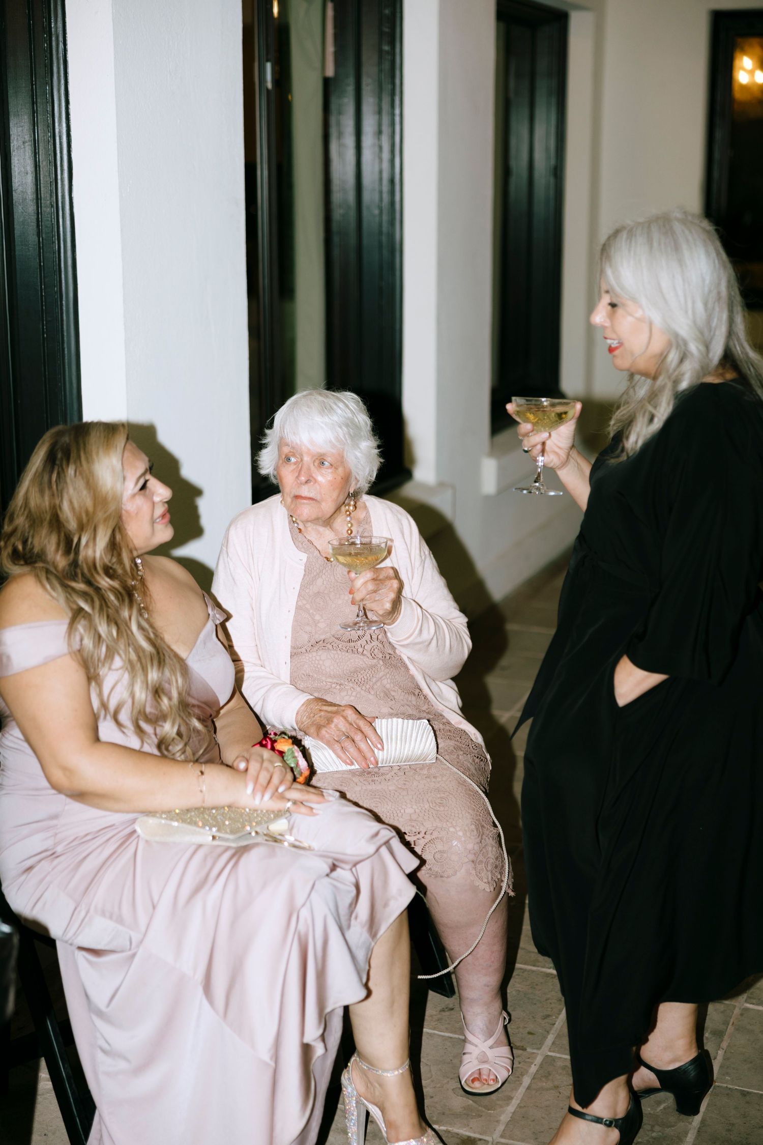 Three guests in formal attire enjoying drinks and conversation at an elegant evening event.