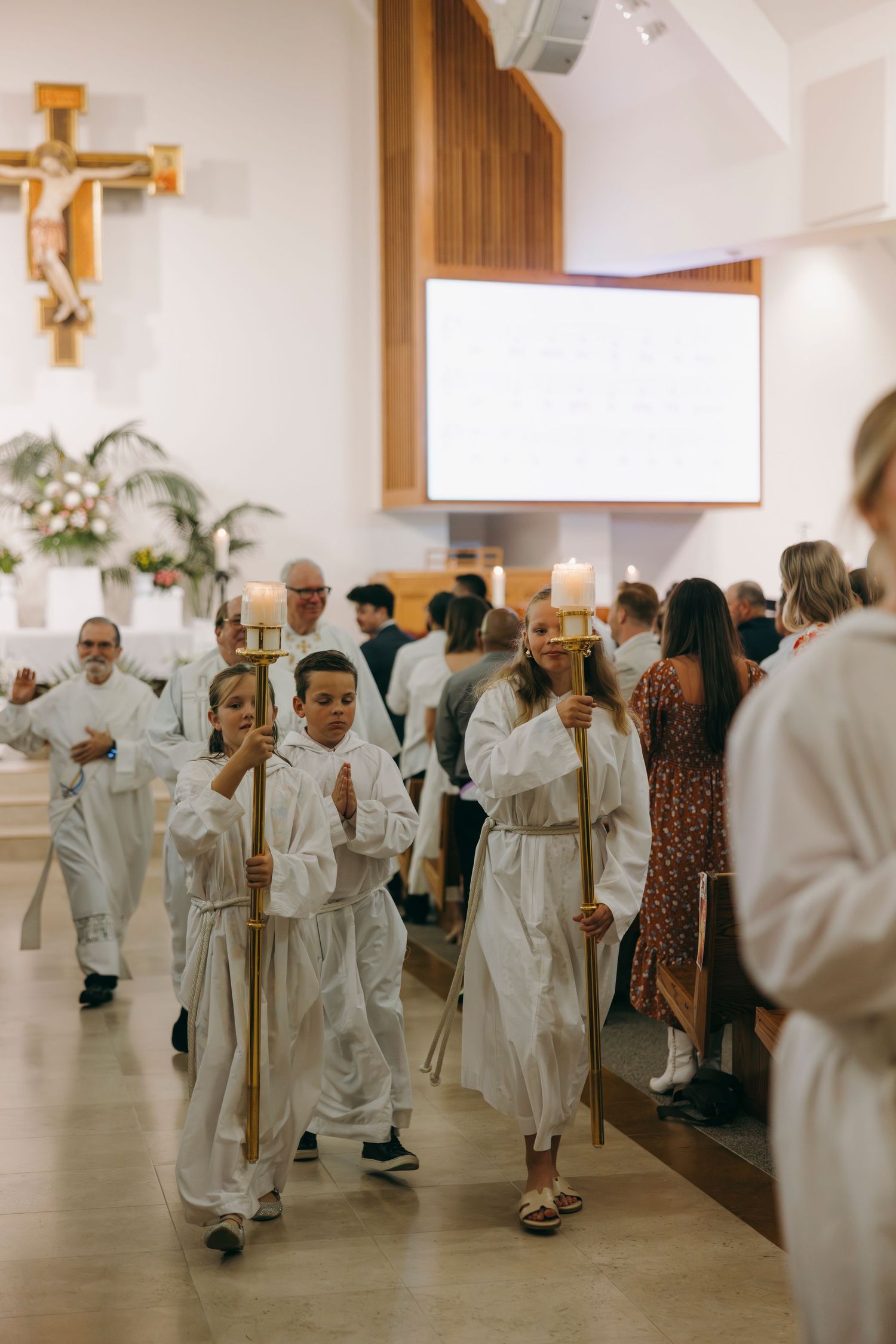 Children in white robes processing with candles during Catholic Easter Vigil Mass ceremony.