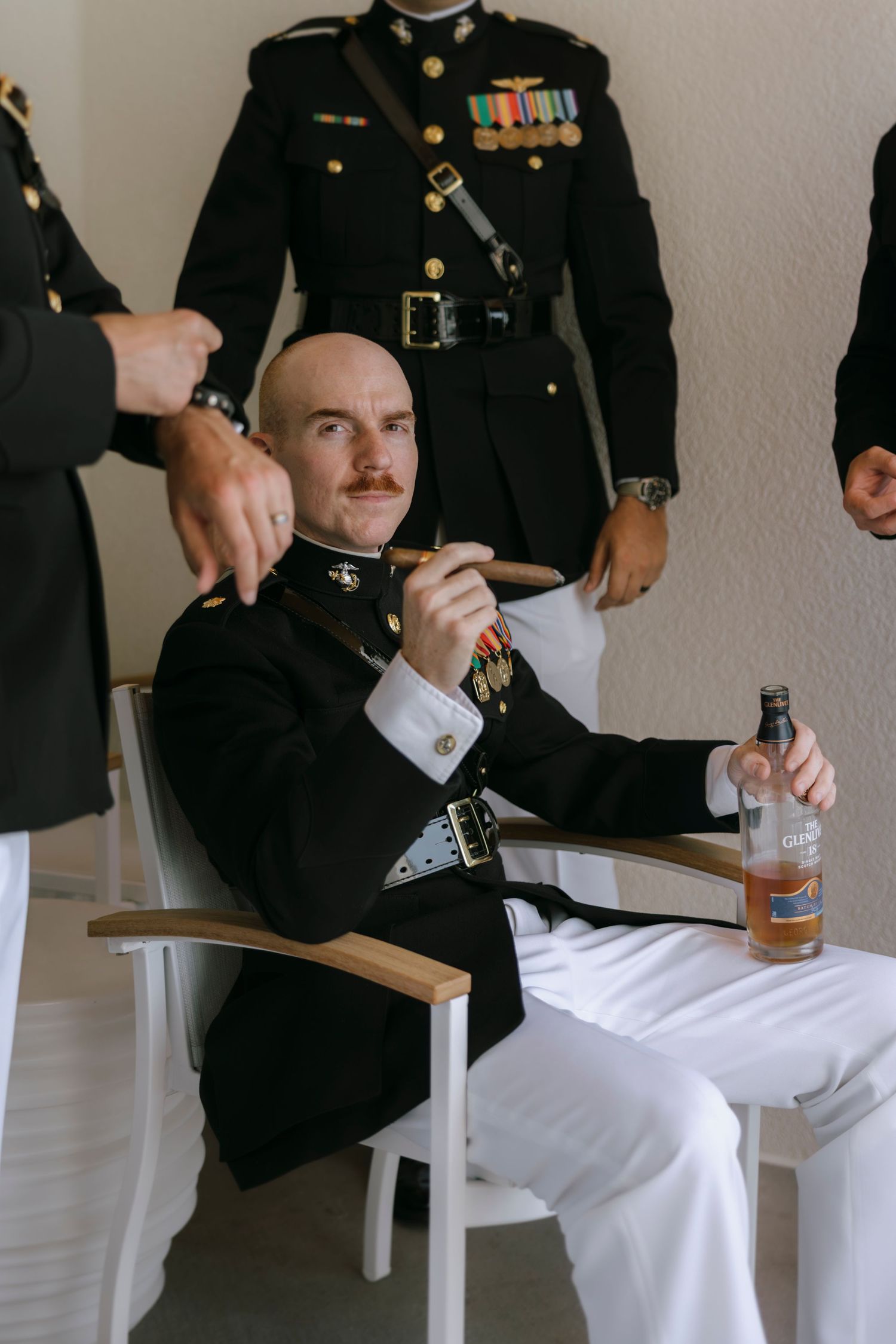 Military officer in dress uniform seated with cigar and whiskey bottle, surrounded by fellow servicemen.