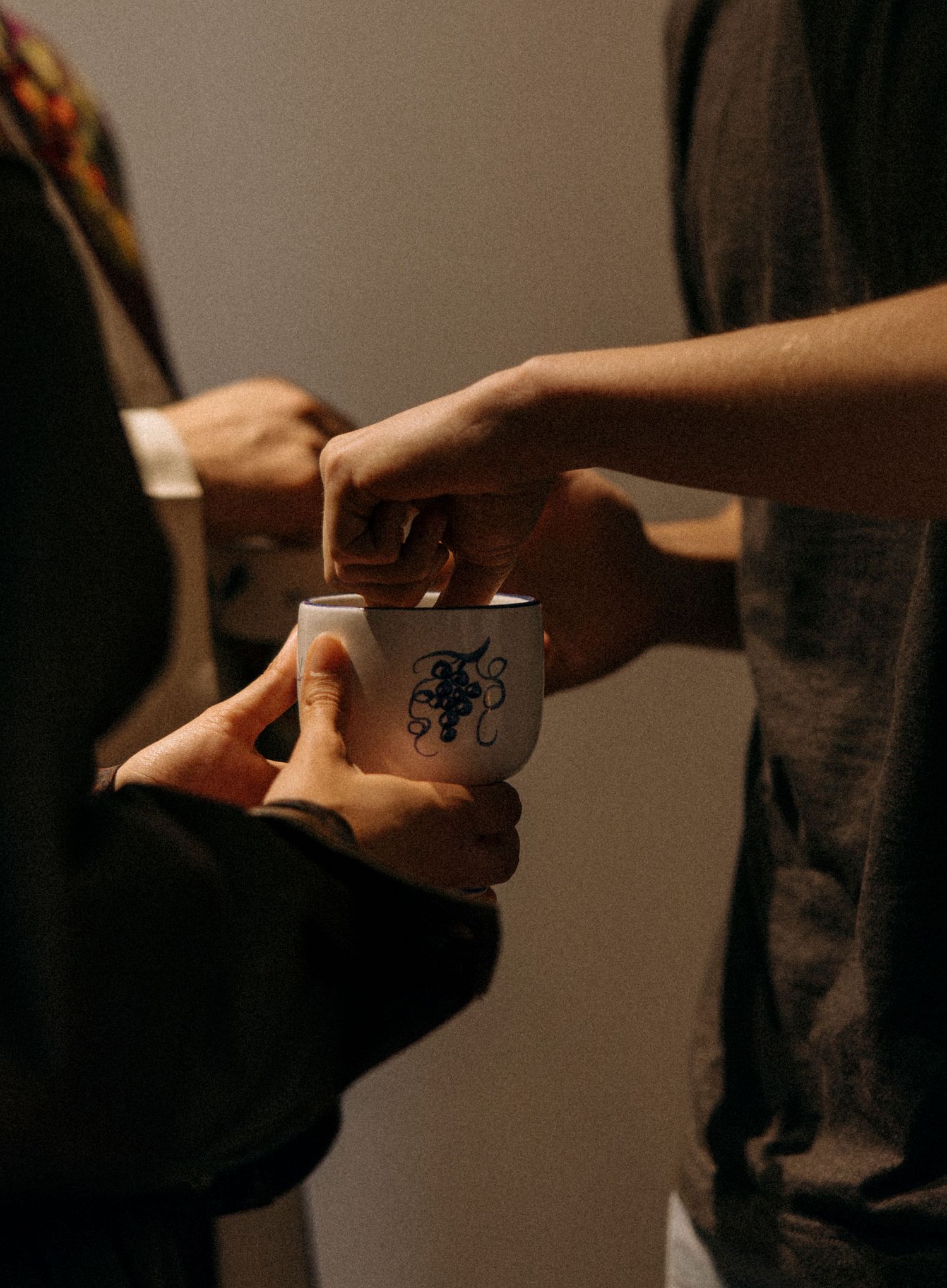 Close-up of hands exchanging a decorative coffee cup in dim lighting.