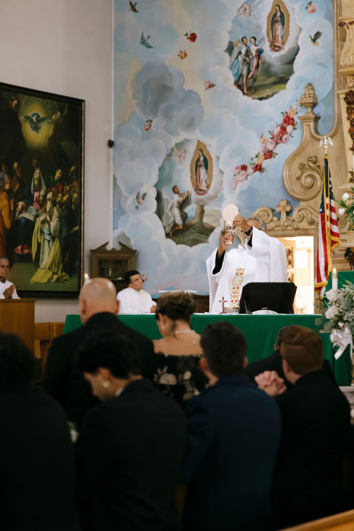 Church interior with ornate ceiling murals and religious artwork during a ceremony.