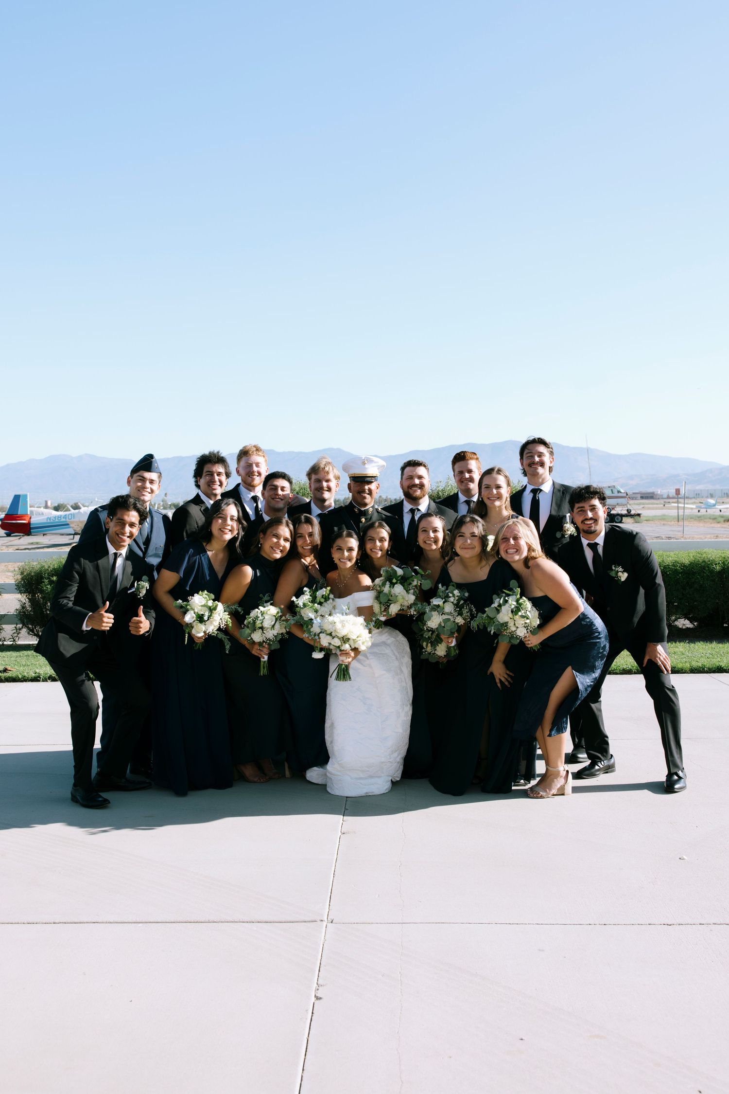 Wedding party members in black attire gather closely for a cheerful group photo.