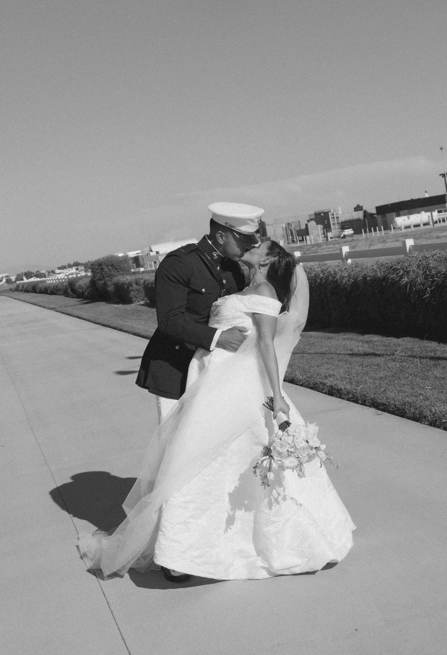 A black and white wedding photo showing a romantic moment on a concrete path.