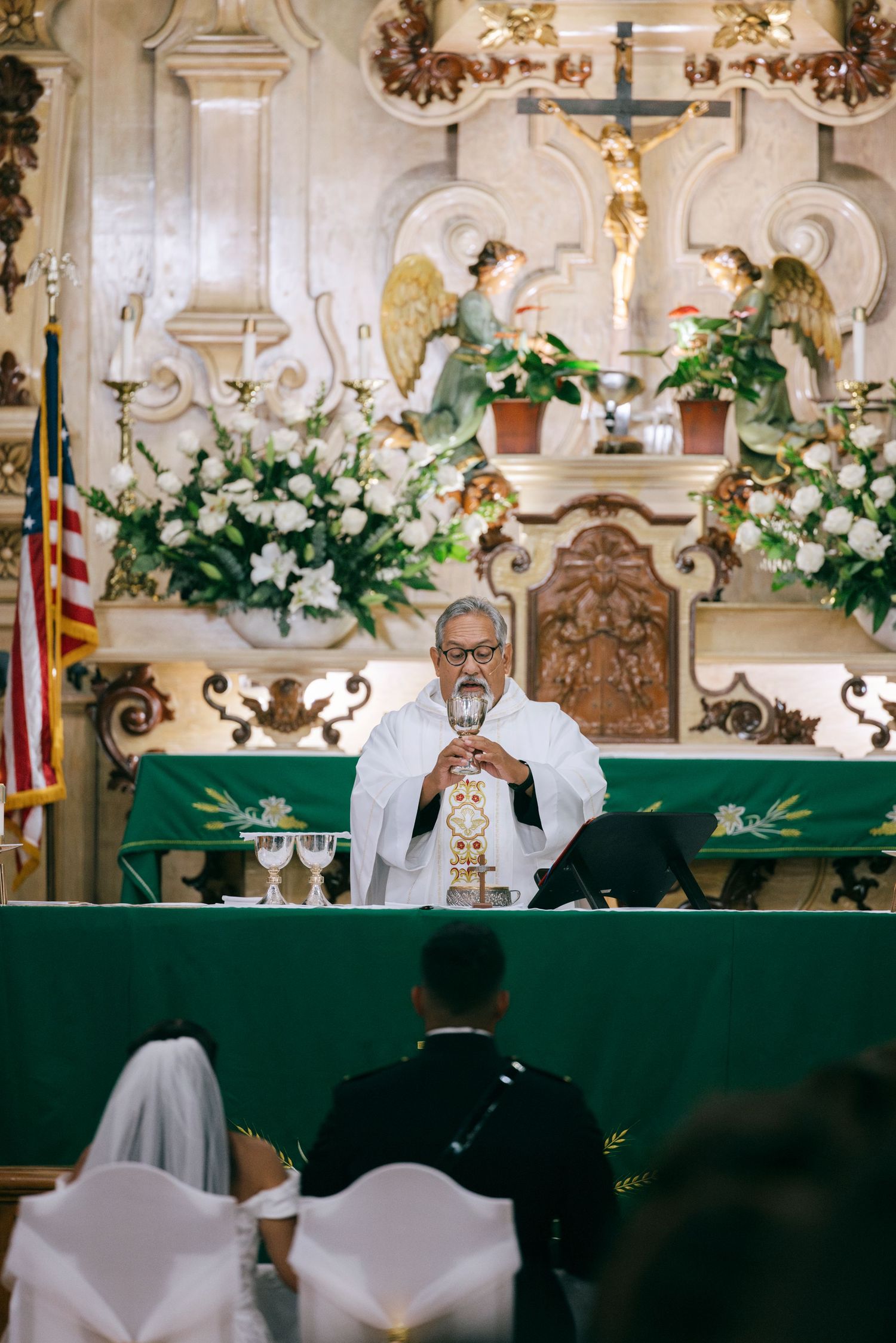 Church altar decorated with white flowers and green altar cloths for a wedding ceremony.