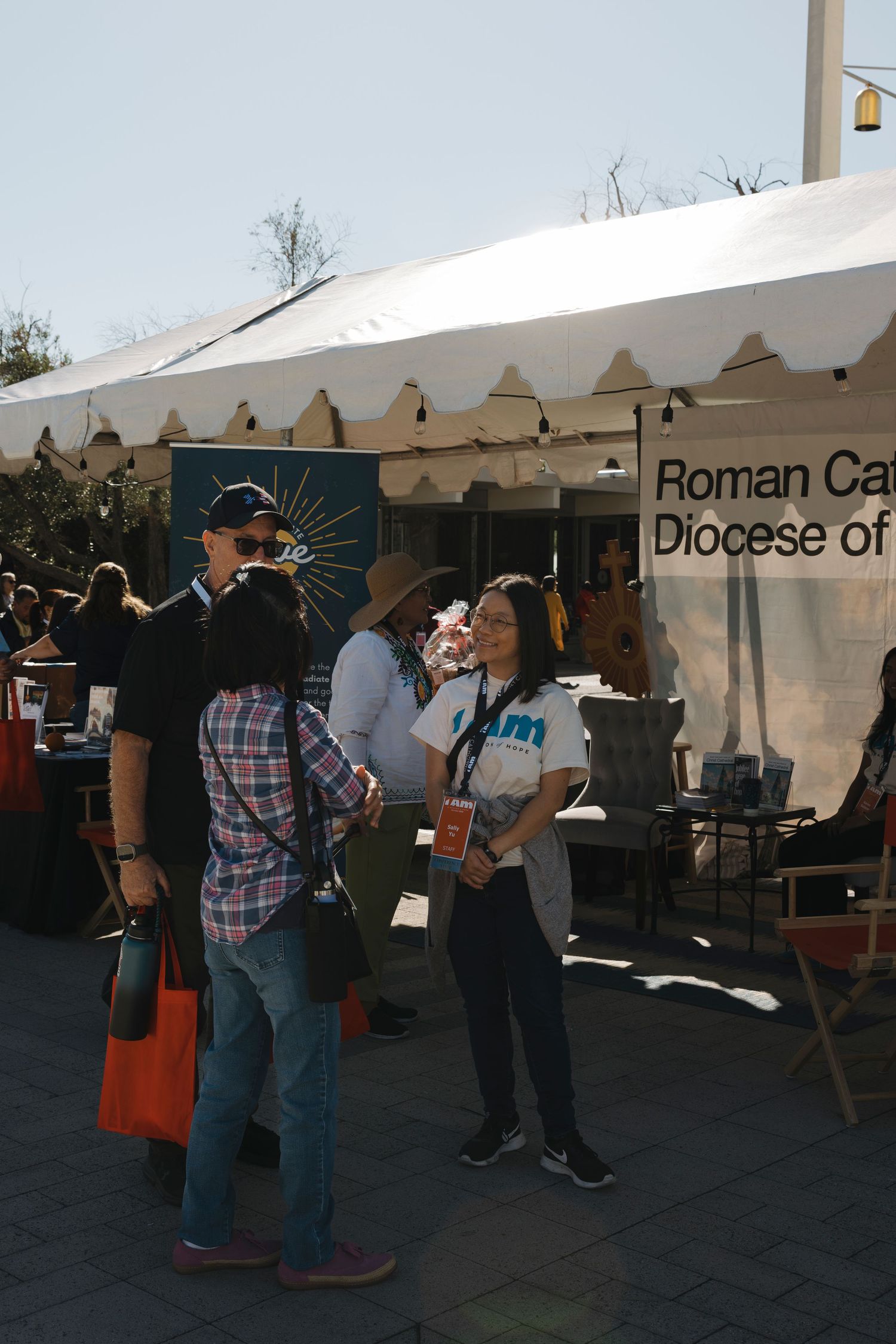 White event tents with Roman Catholic Diocese signage and attendees browsing displays.