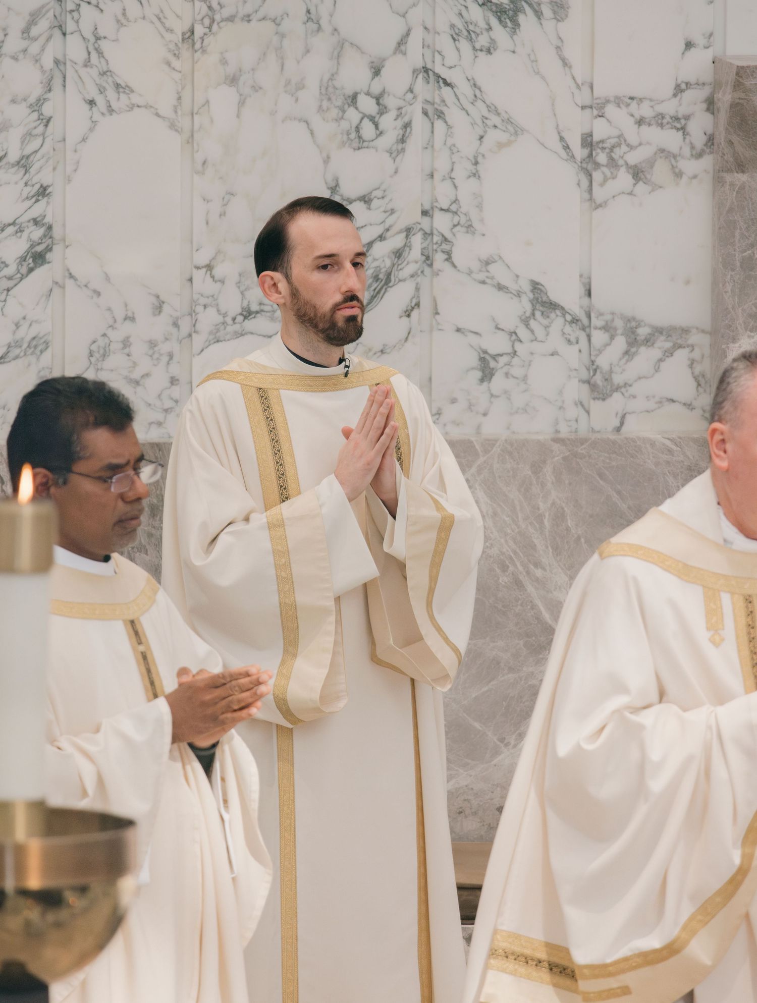 Clergy members in white and gold vestments standing in prayer during religious service.