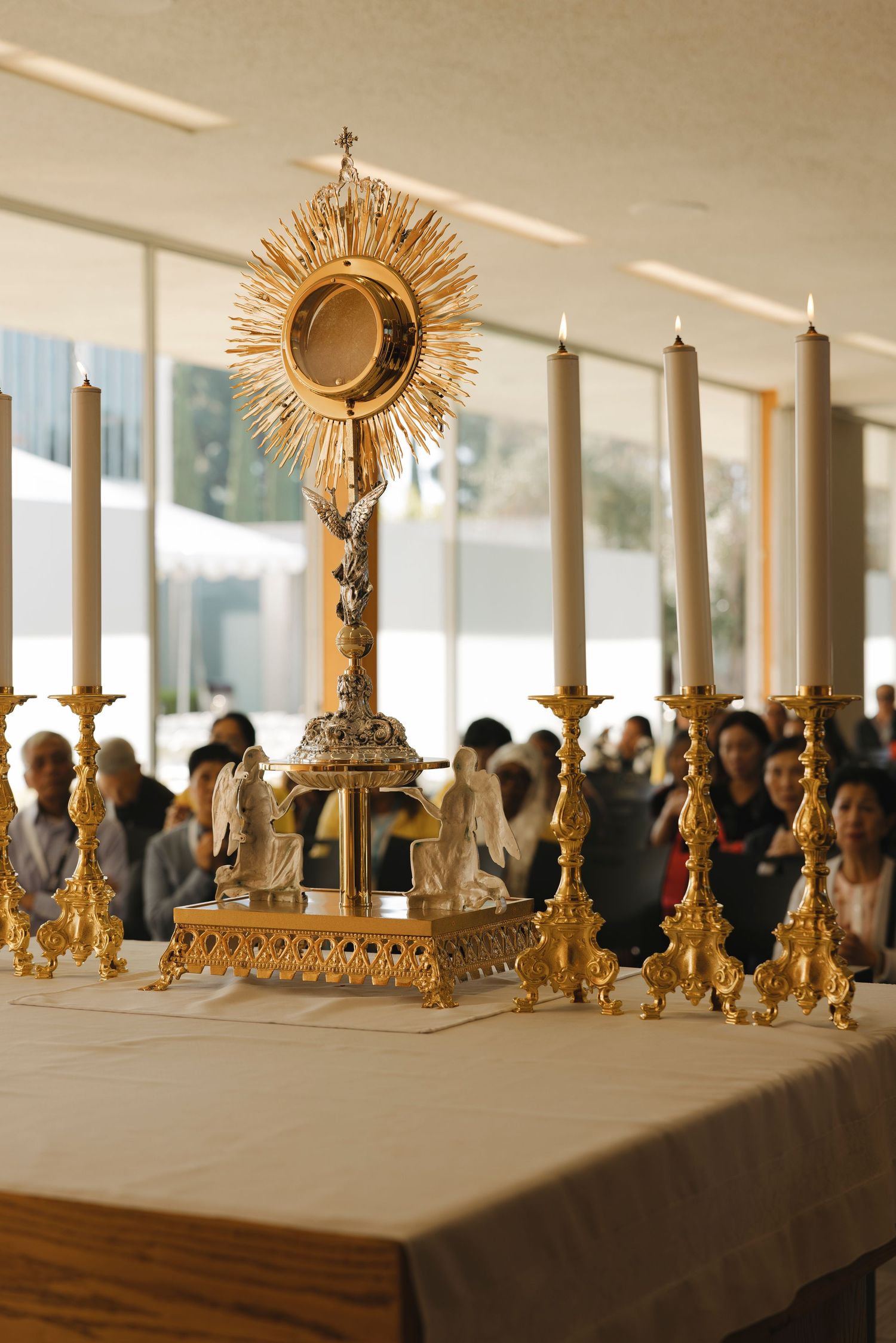 Golden religious artifacts and candelabras displayed on a table with crowd in background.
