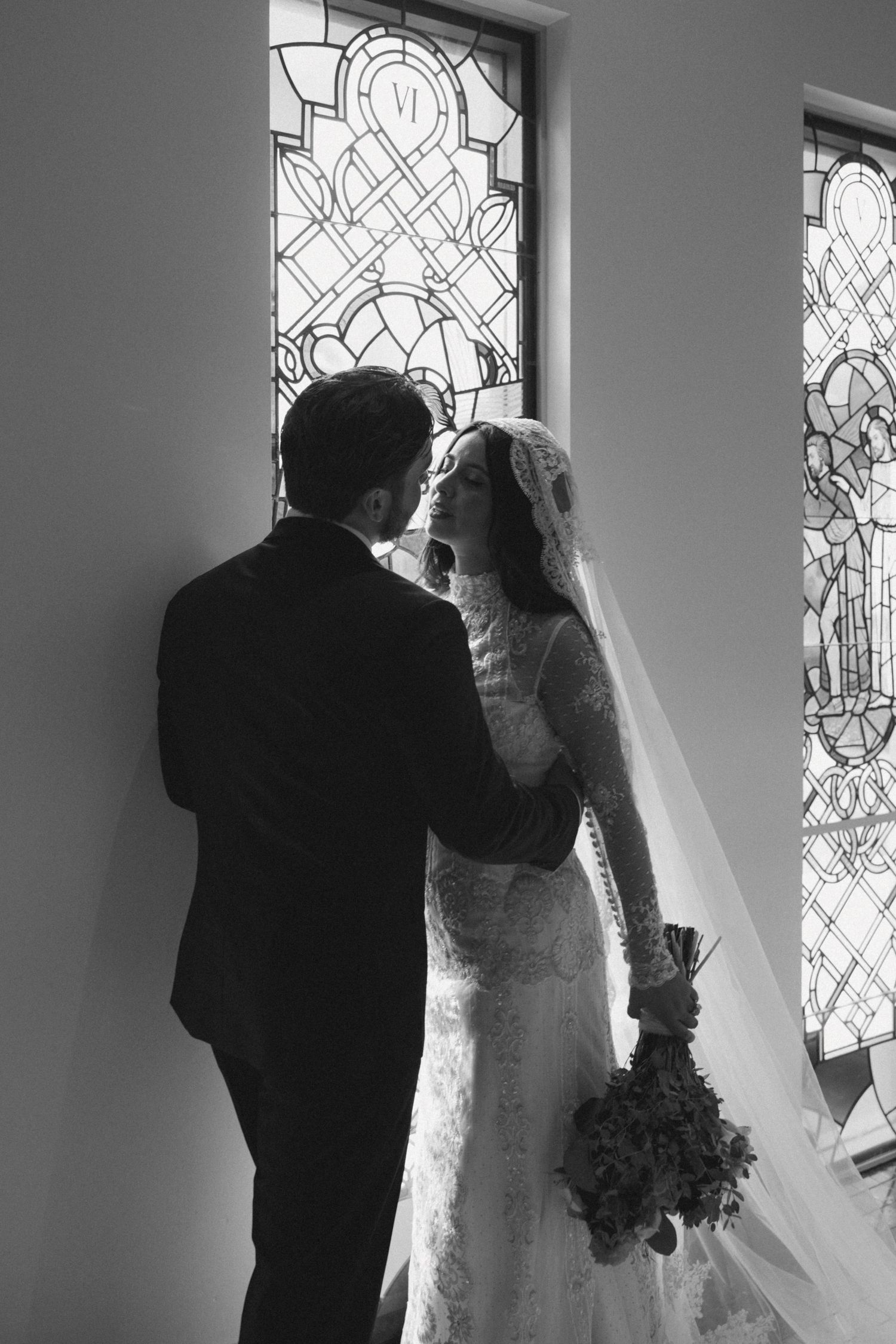 A black and white photo of a couple silhouetted against church stained glass windows.