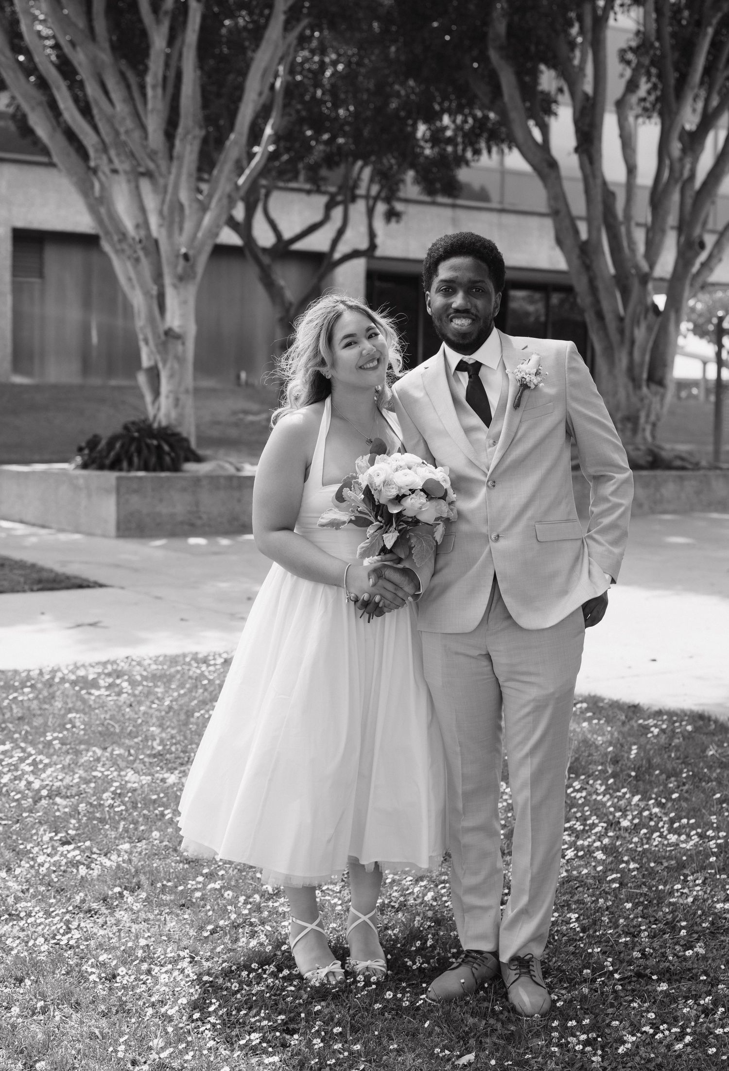 Black and white portrait of newlyweds laughing together outdoors on their wedding day.
