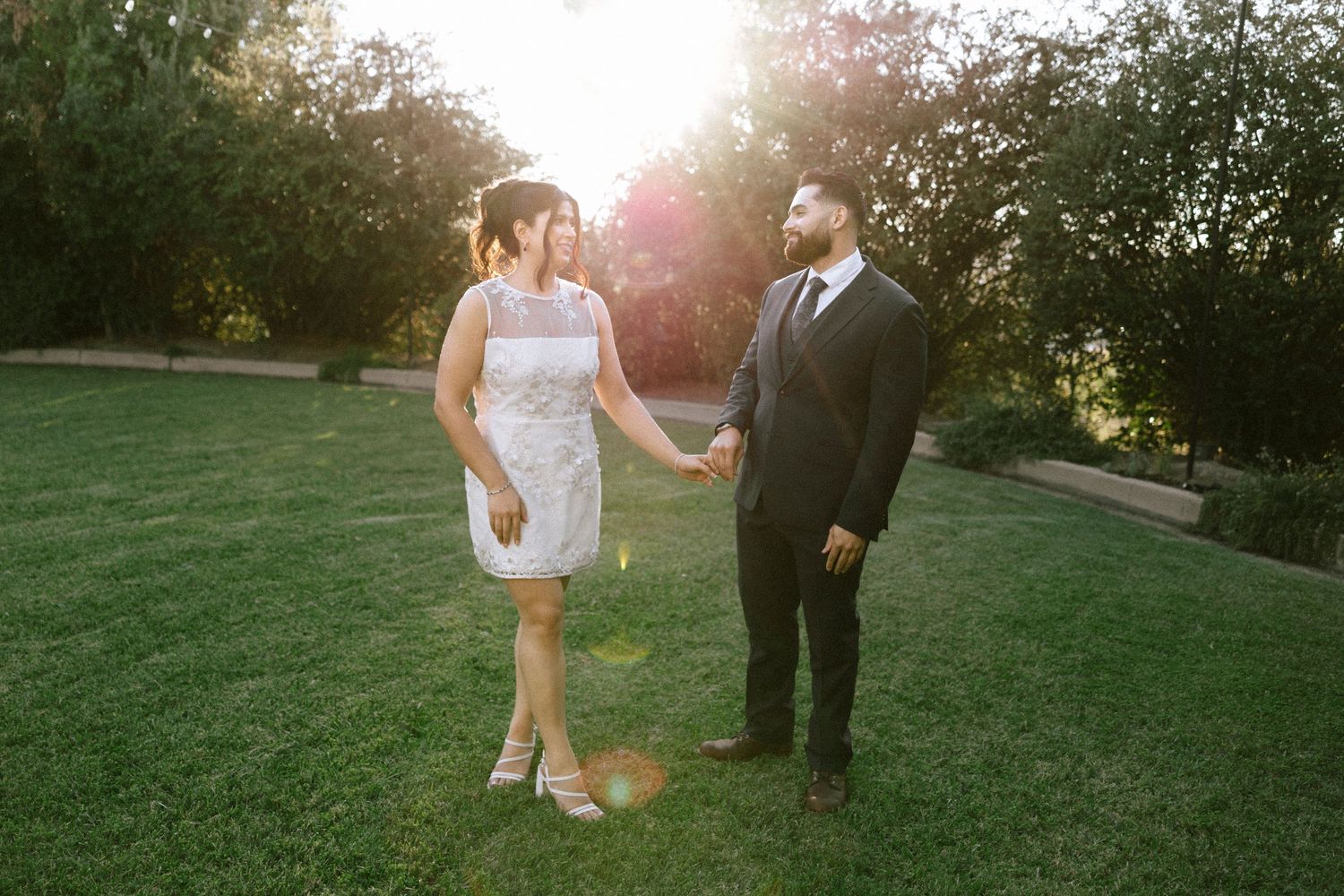 A couple poses together on a grassy lawn during golden hour sunset.