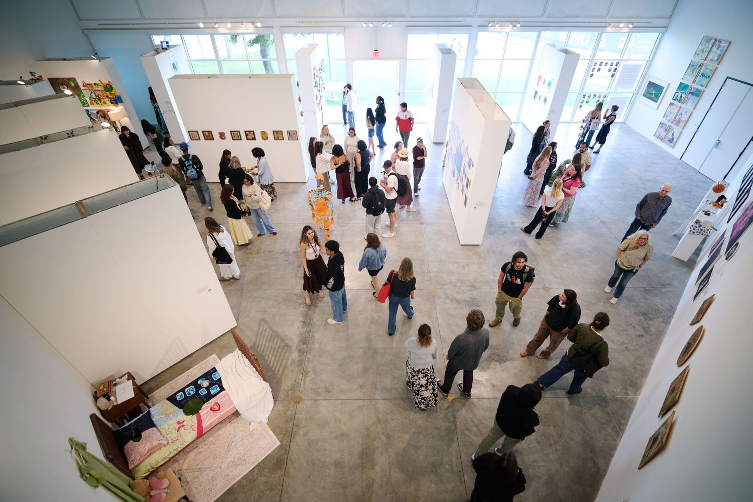 Aerial view of visitors browsing artwork at a busy art gallery opening event with high ceilings and natural light.