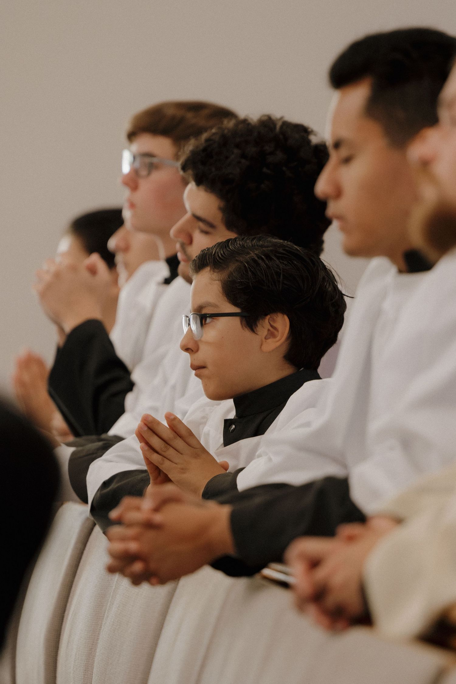 Young men in white shirts sit in a row during a religious service.