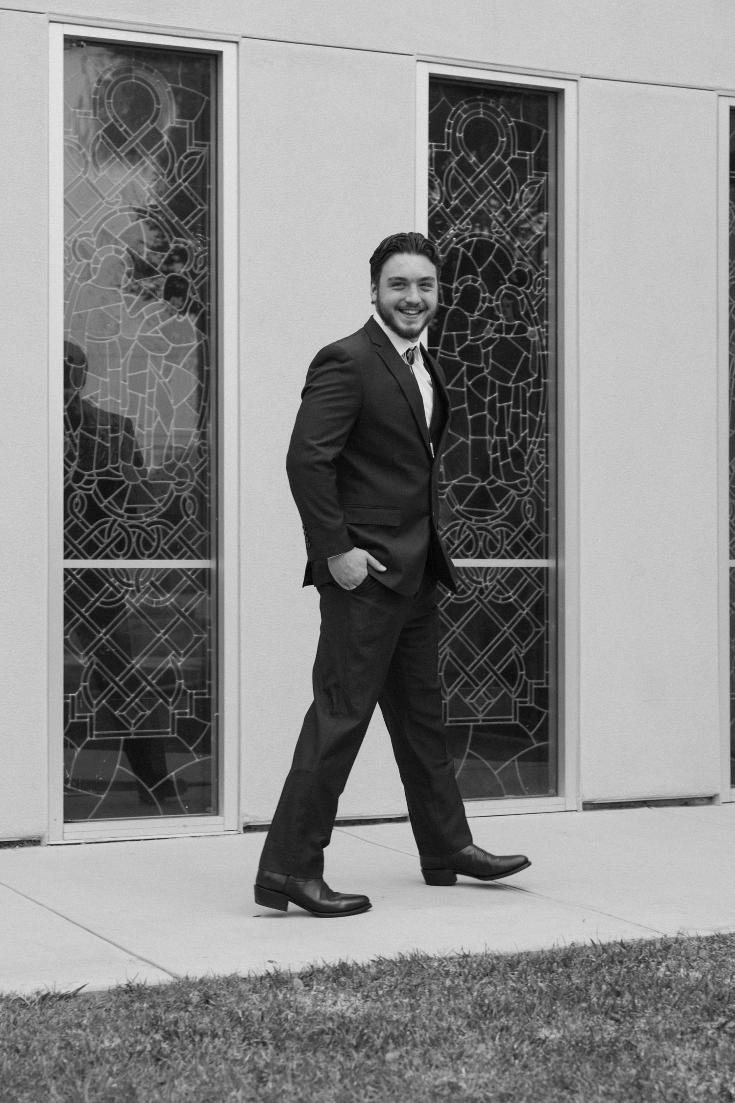 Person in business suit poses confidently by geometric patterned windows in black and white.