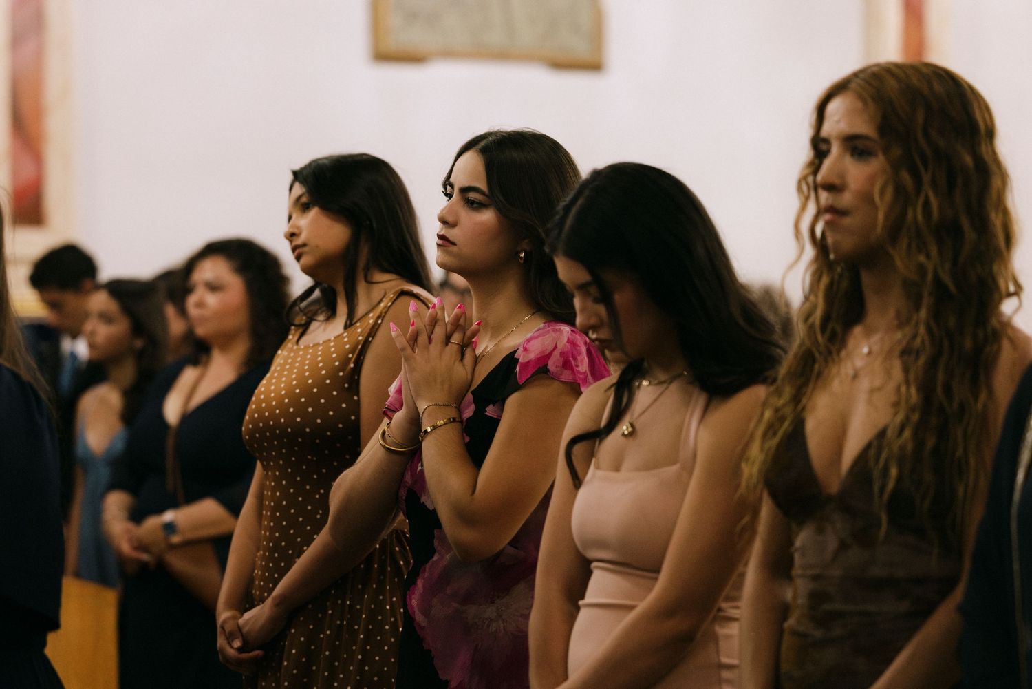 Wedding guests stand in formal attire during a church ceremony.