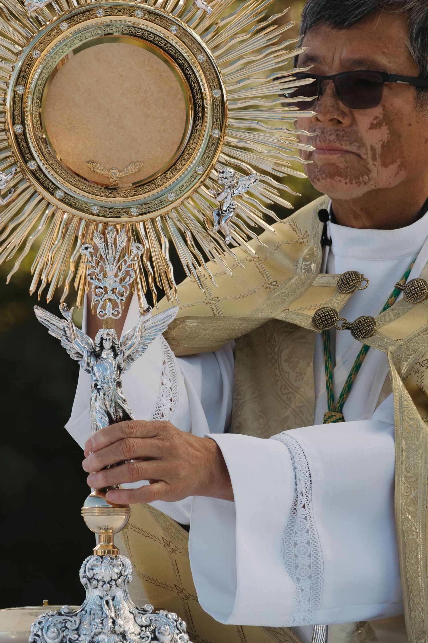 Close-up view of priest holding ornate golden monstrance during Catholic benediction ceremony.