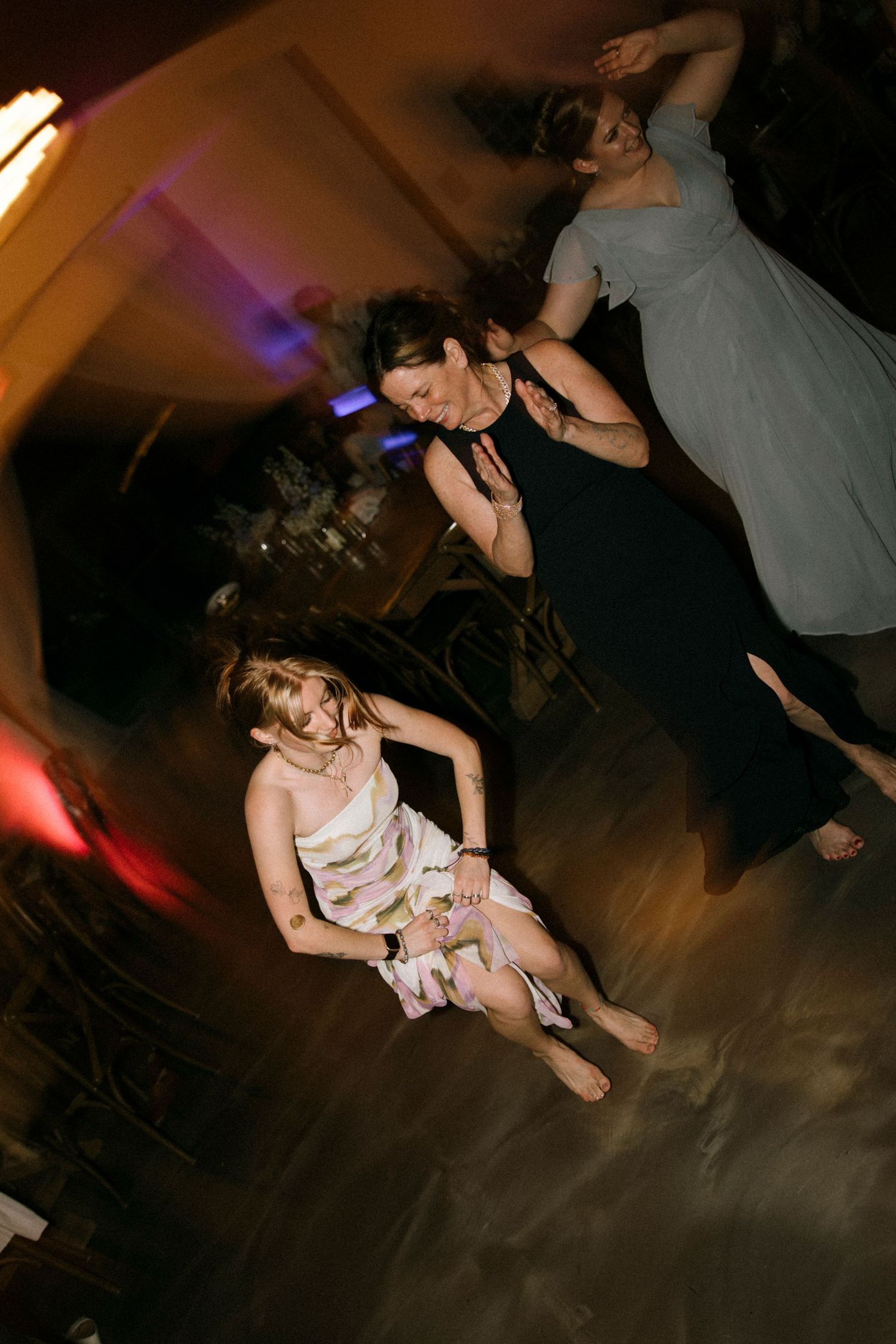 Women dancing at a party, shot from above, with colorful ambient lighting in a dimly lit venue.