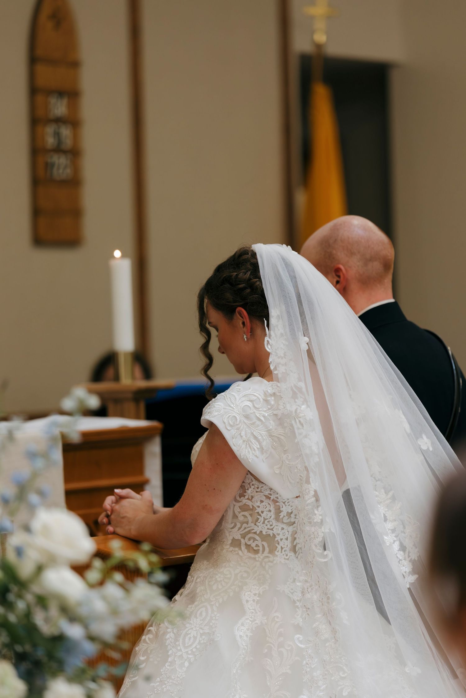 Bride and groom kneeling at church altar during wedding ceremony, bride wearing lace gown and veil.