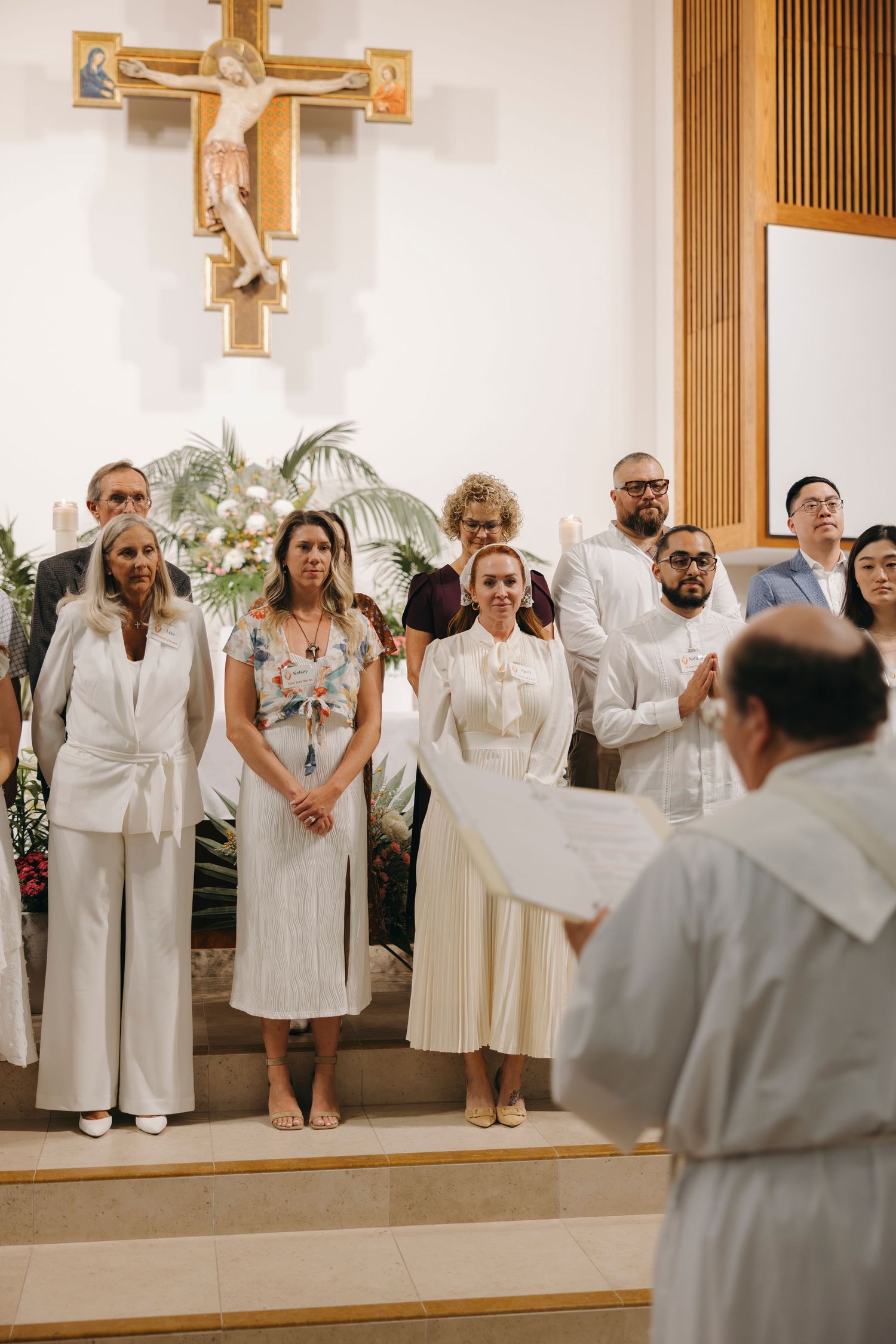 Group in white attire standing before a priest at a church altar ceremony.