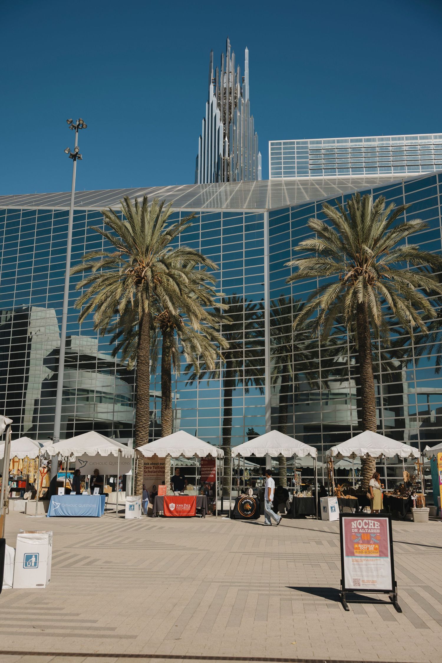Modern glass church building with palm trees and vendor tents outside on a sunny day.