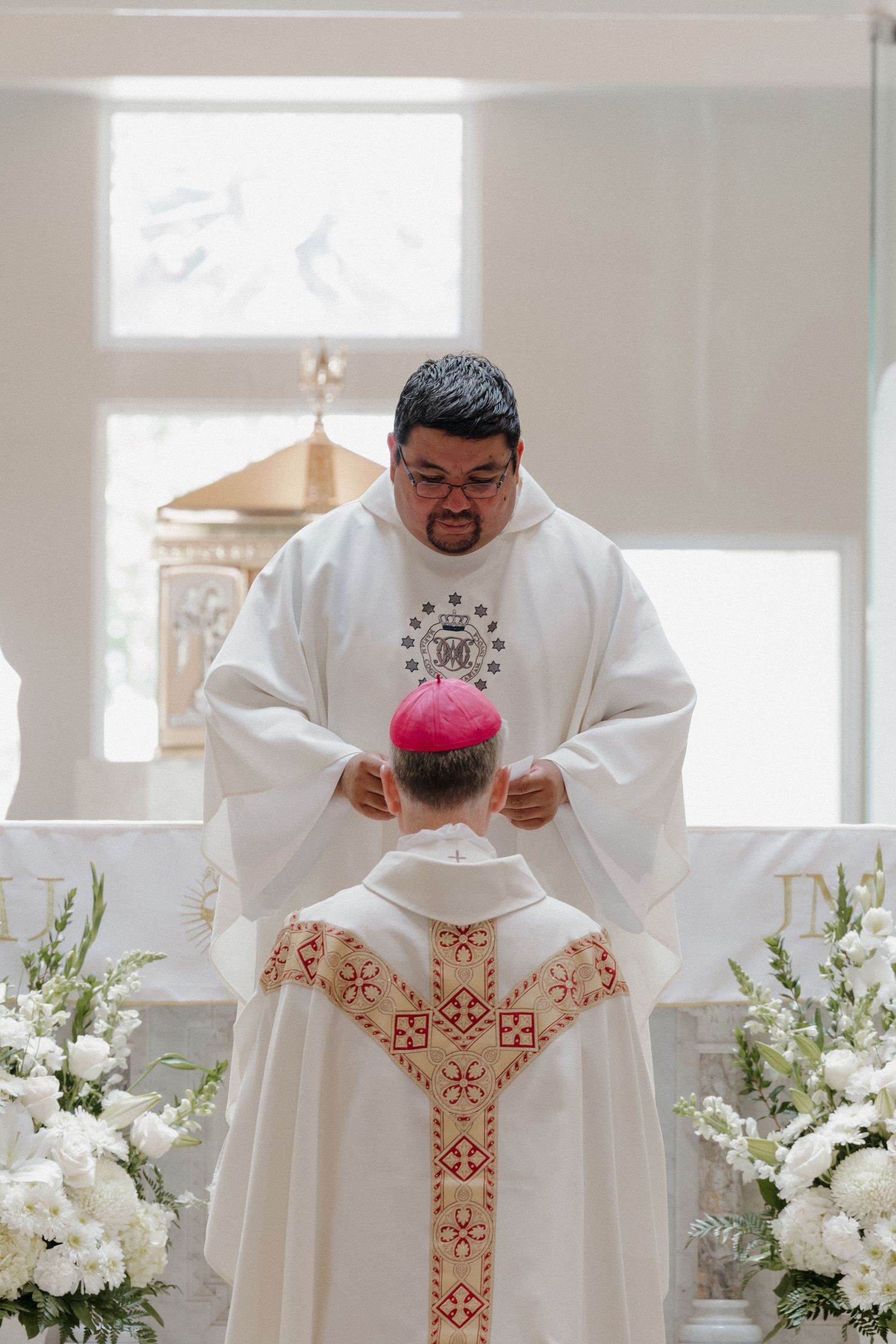 Clergy in white robes performing a religious ceremony at an altar with floral decorations.