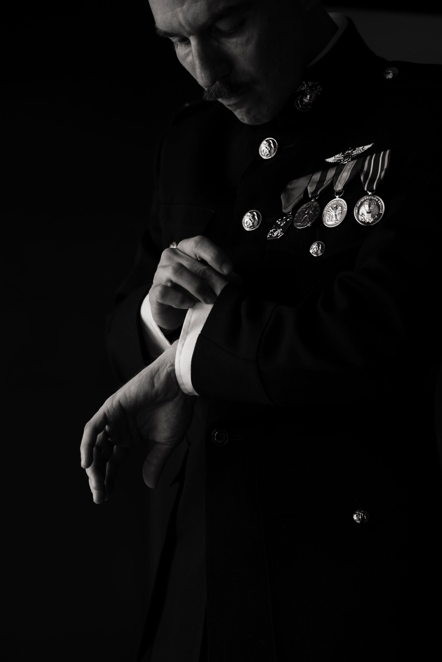 Black and white portrait of a military officer in dress uniform adjusting cufflinks, medals displayed on chest.