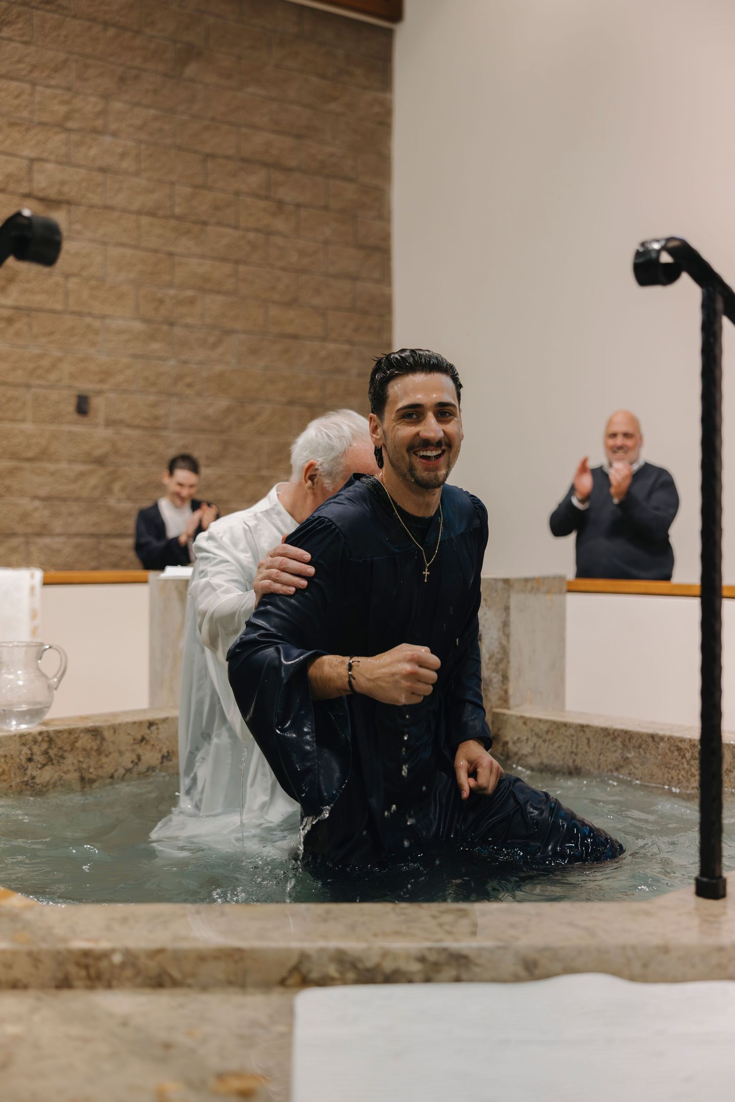 Smiling man emerging from baptismal waters during adult Catholic baptism ceremony in church.
