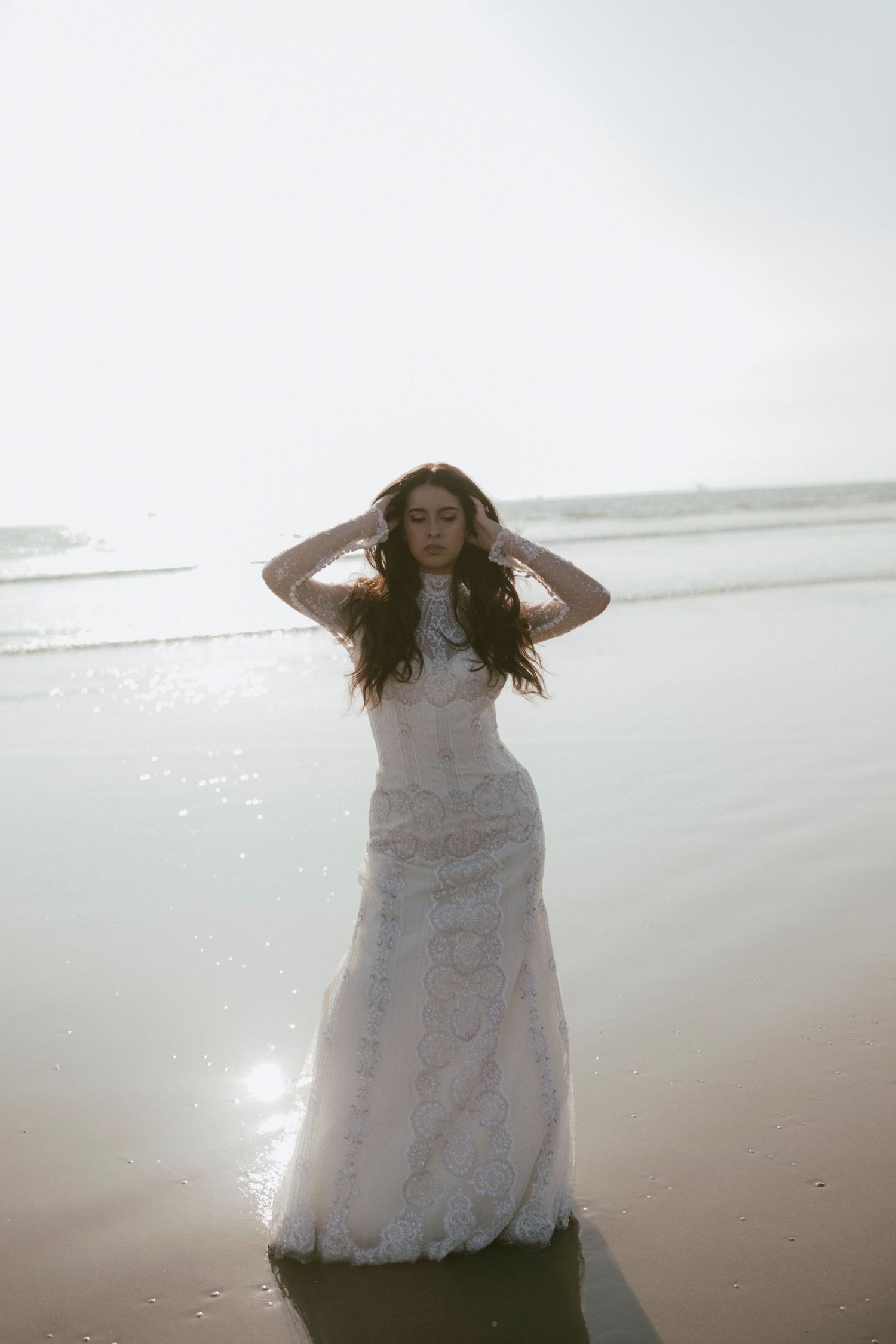 Bride in lace dress posing on beach with wind blowing through her hair.