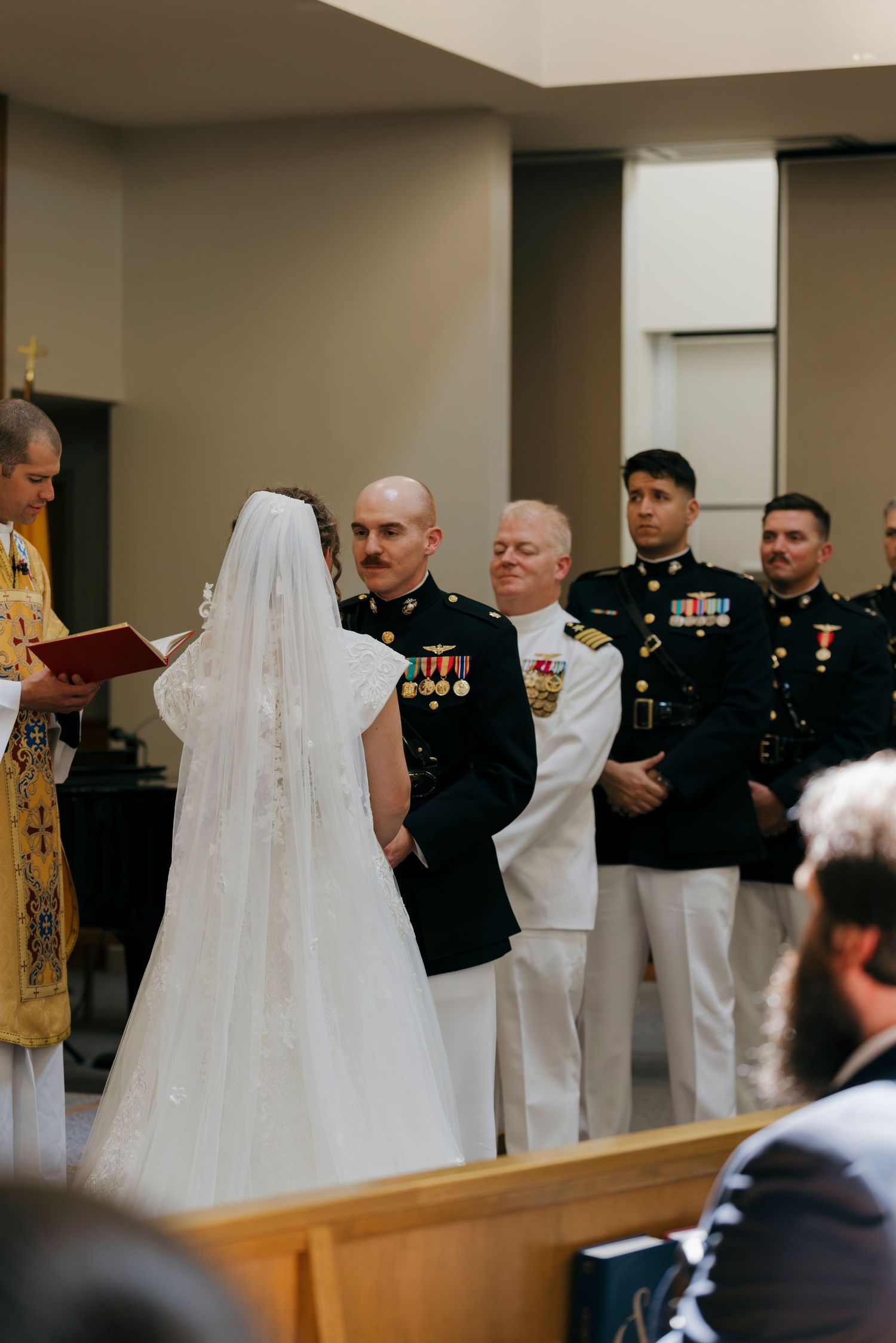Military wedding ceremony in church with bride in white gown and groom in dress uniform flanked by groomsmen.