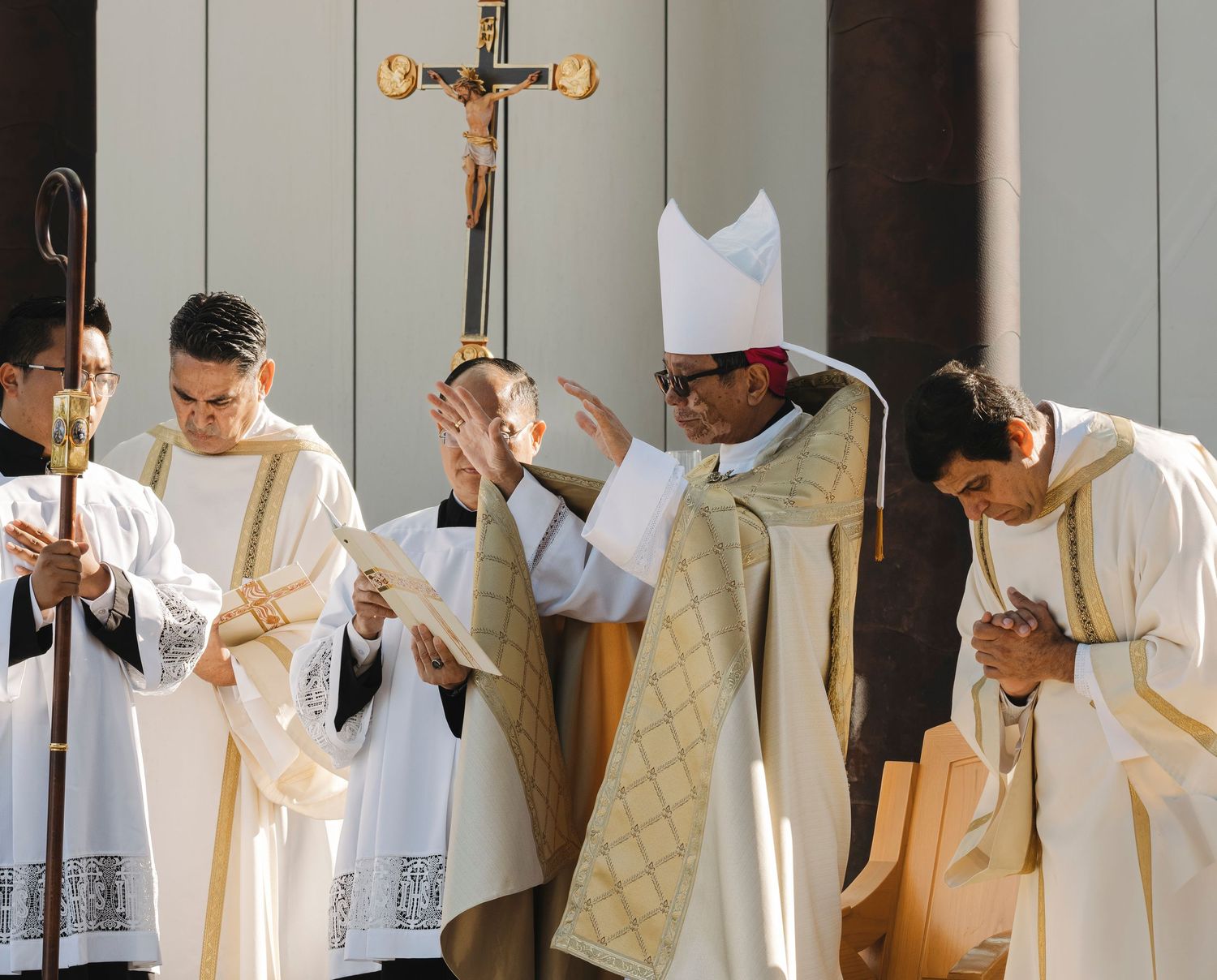 Priests and altar servers in white and gold vestments process in formation during a religious service.