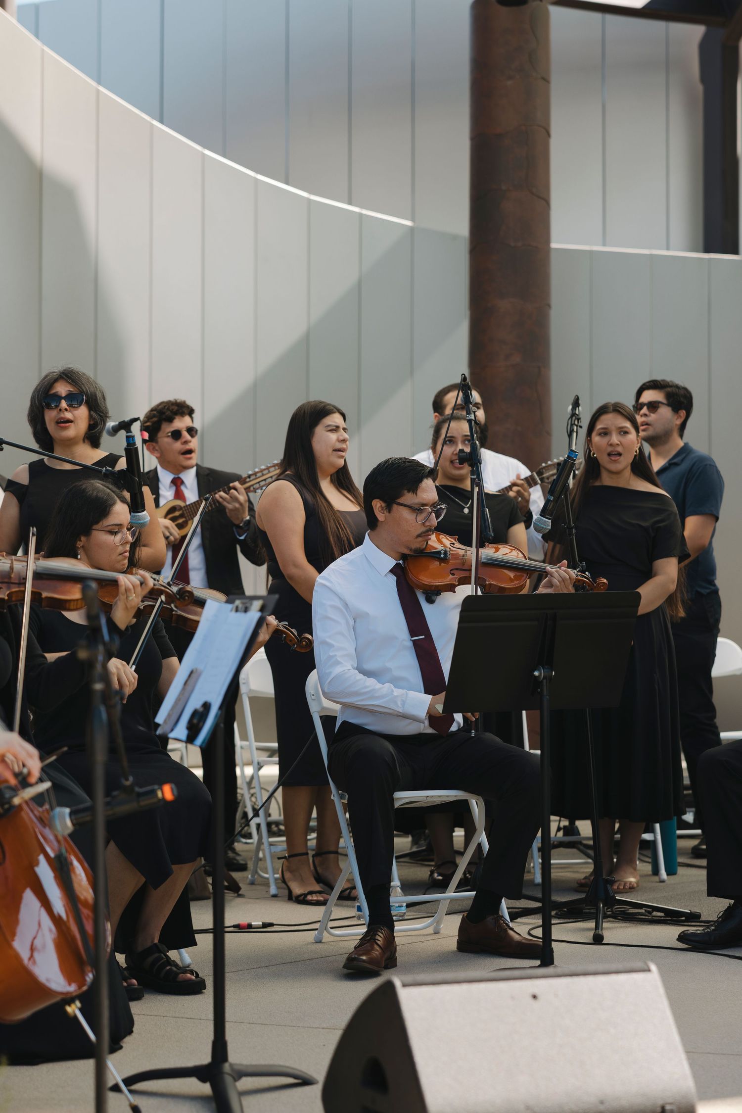 Orchestra members performing in a modern venue with white walls and wooden beams.