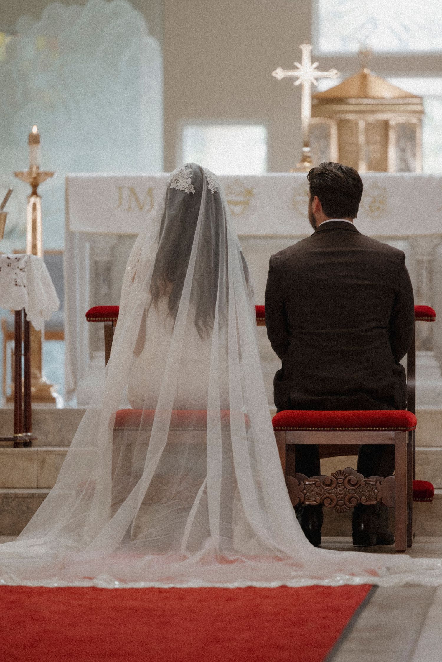 Wedding ceremony view showing long white veil against red carpet in church setting.