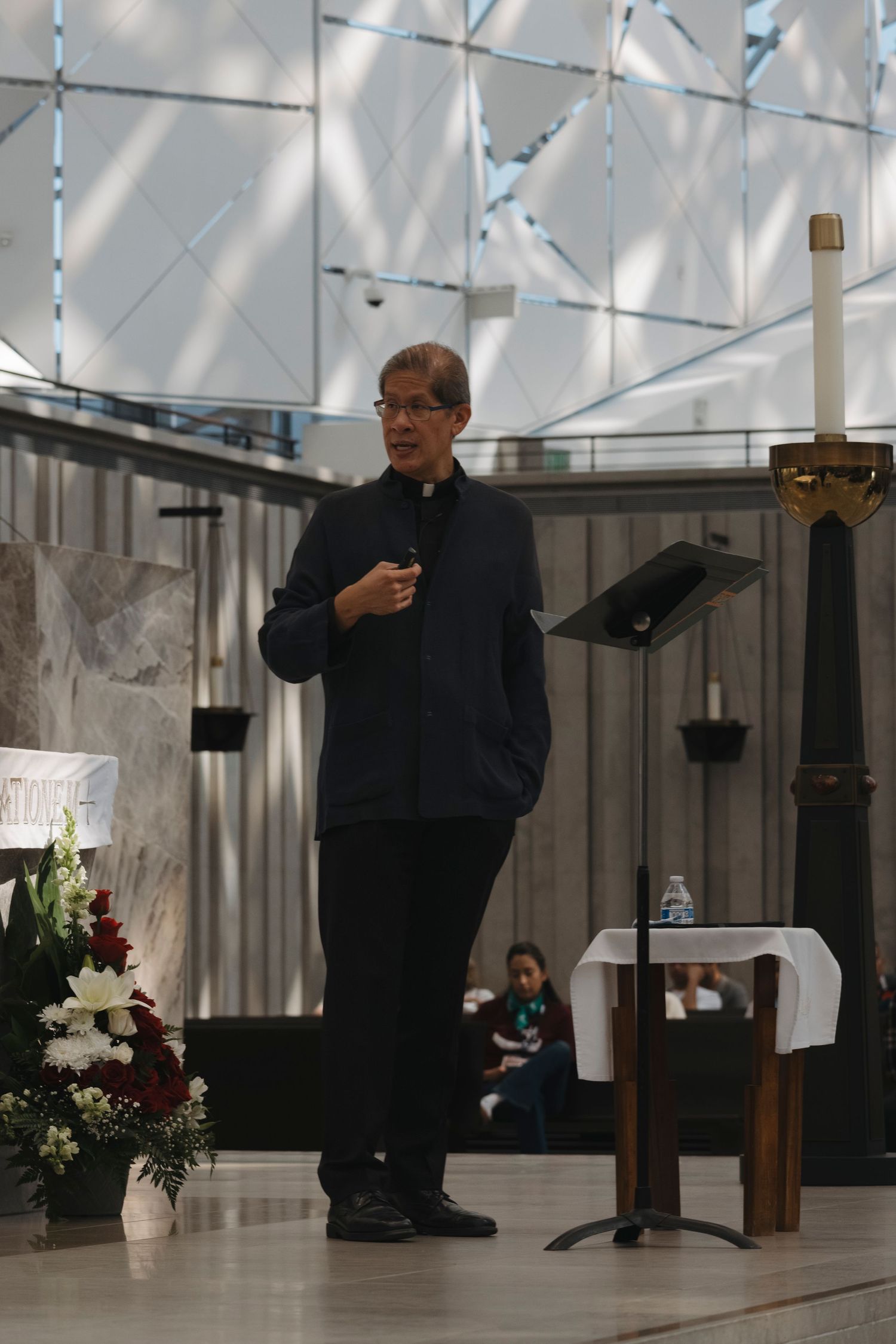 Speaker gesturing while giving a presentation at a wooden podium in a well-lit venue.