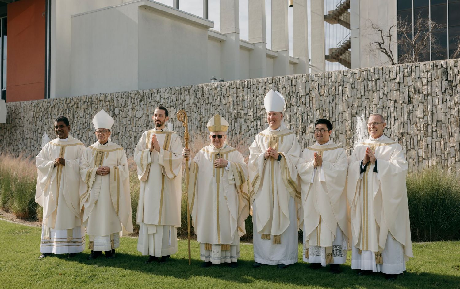 A wide shot of religious leaders in white robes lined up against a modern building exterior.