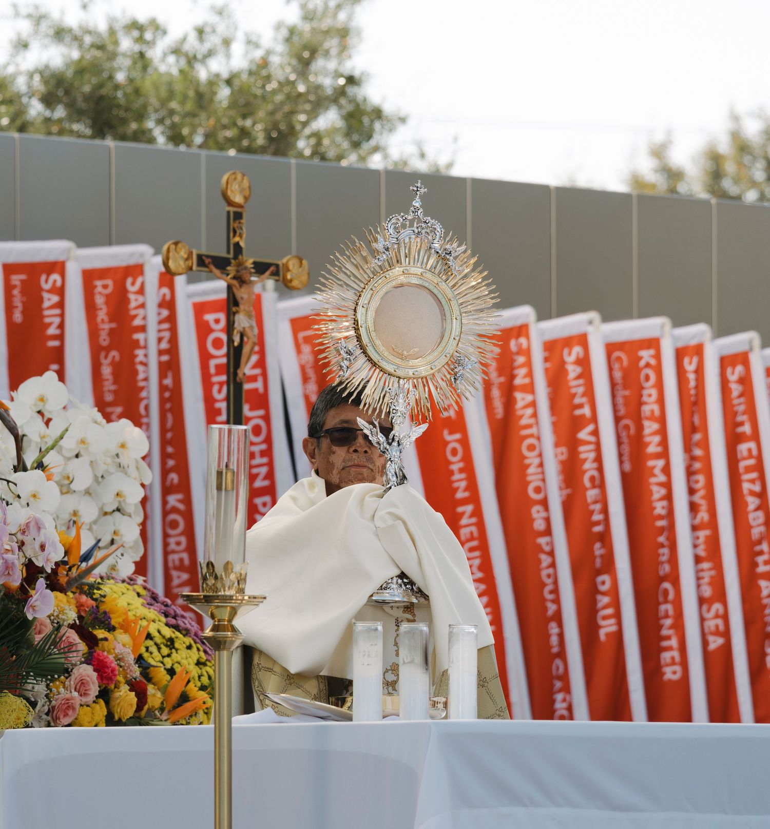 Red banners and religious decorations line an outdoor Catholic ceremony space.