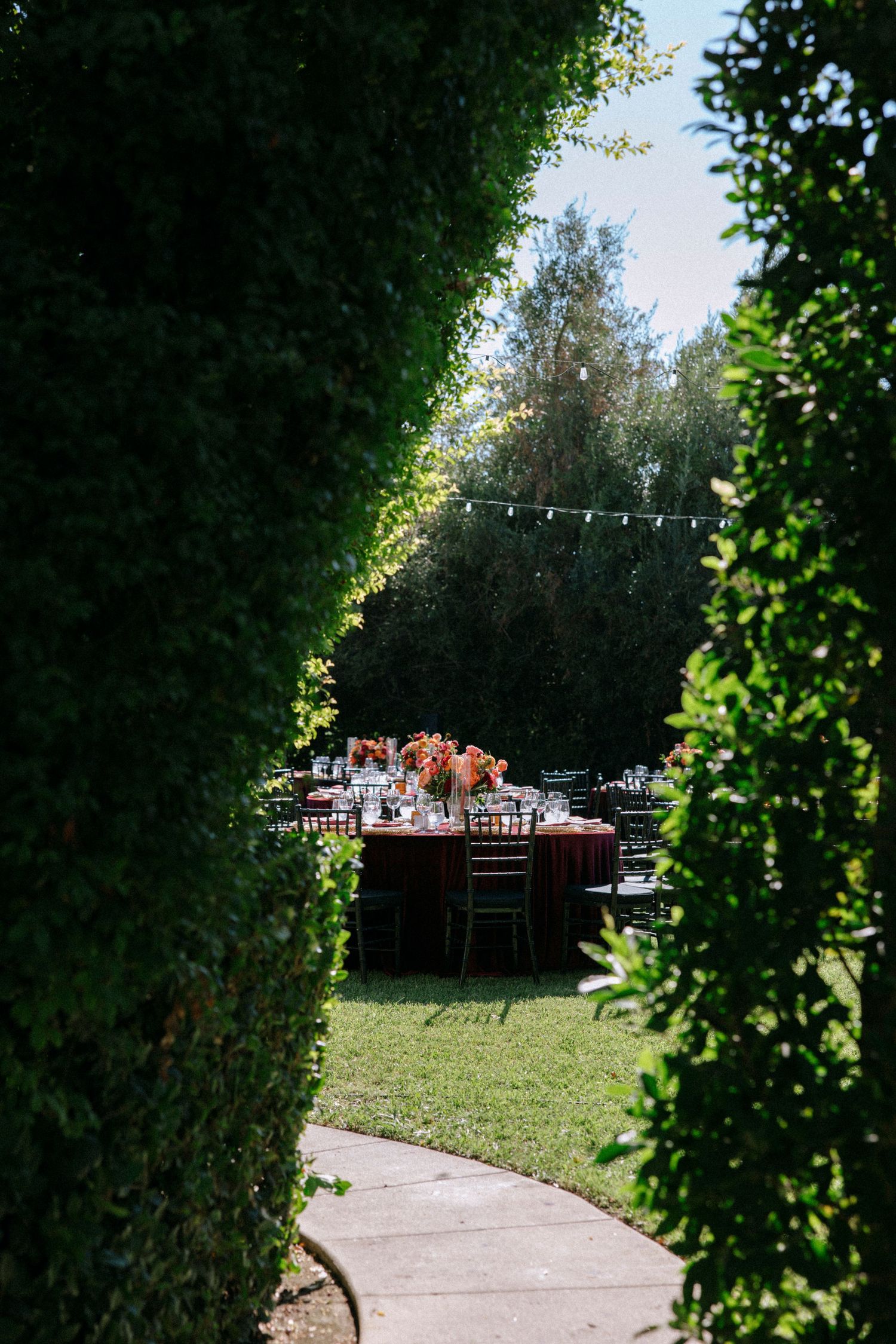 Garden pathway leading to an outdoor wedding reception setup with string lights and greenery.