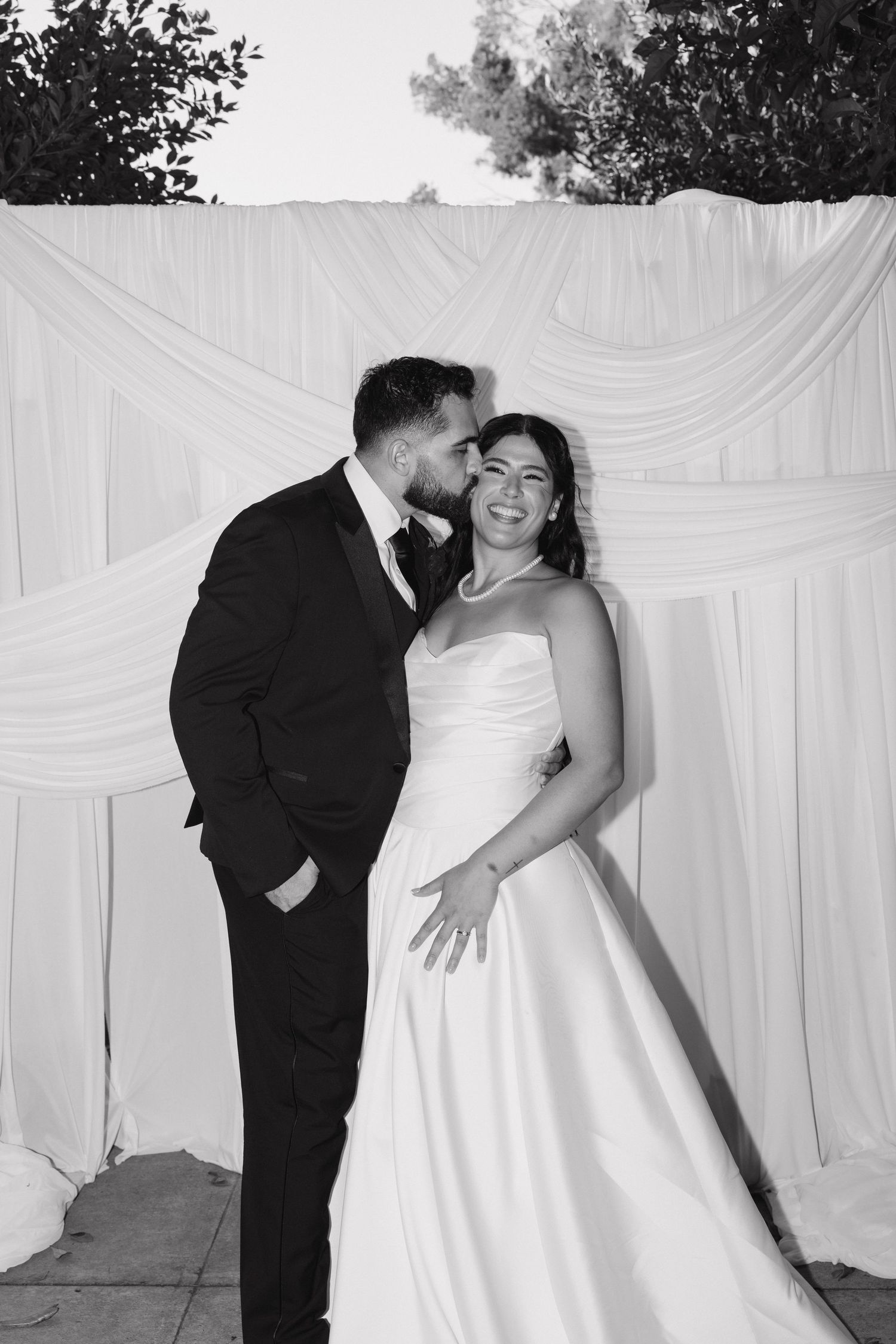 Black and white portrait of a newlywed couple sharing a tender moment against draped fabric.