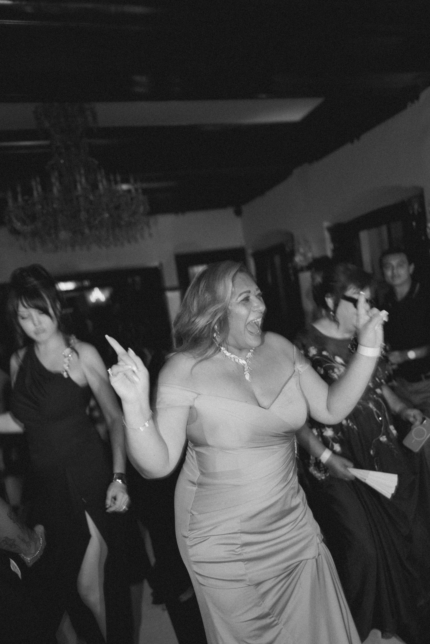 Party guest dancing enthusiastically at an evening celebration with chandelier in background.