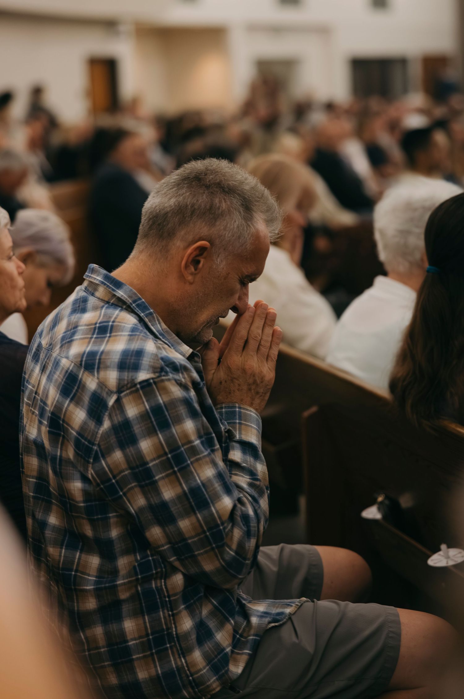 Man in plaid shirt praying with hands clasped during a church service.