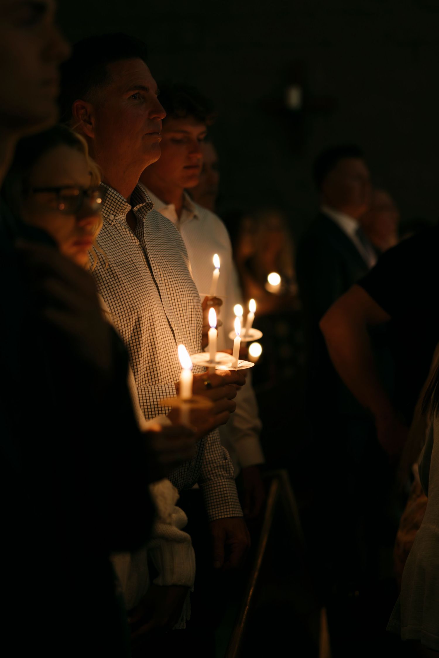 Congregation holding lit candles during Catholic Easter Vigil service in darkened church.