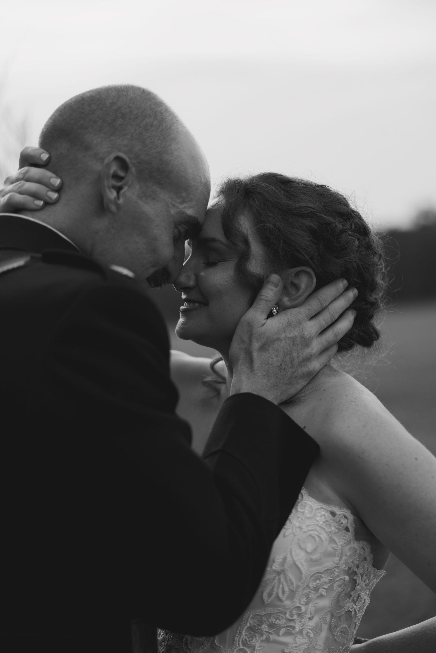 Black and white photo of a smiling bride and groom sharing an intimate moment, foreheads touching at their wedding.