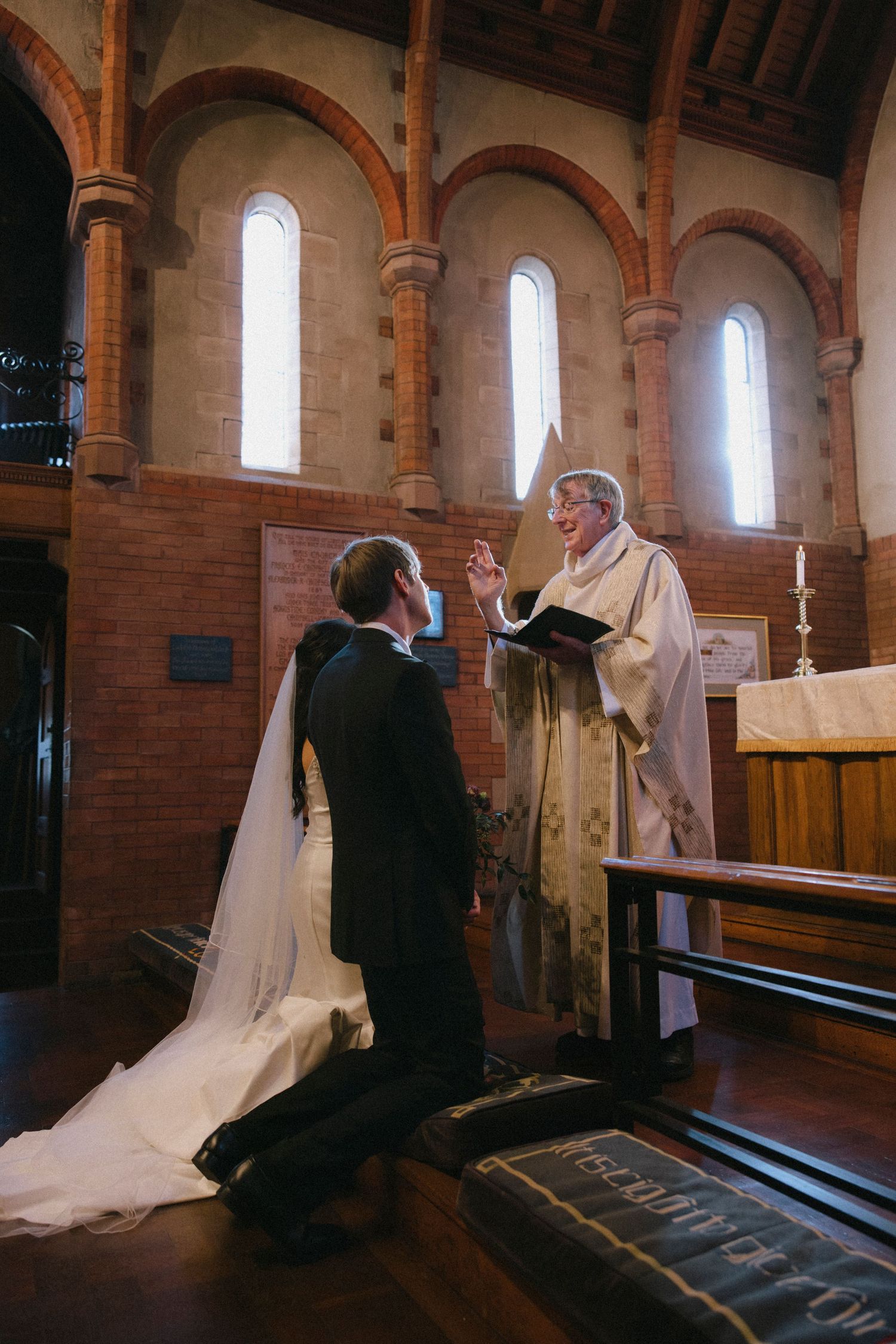 A couple kneels before a priest during a traditional church wedding ceremony.