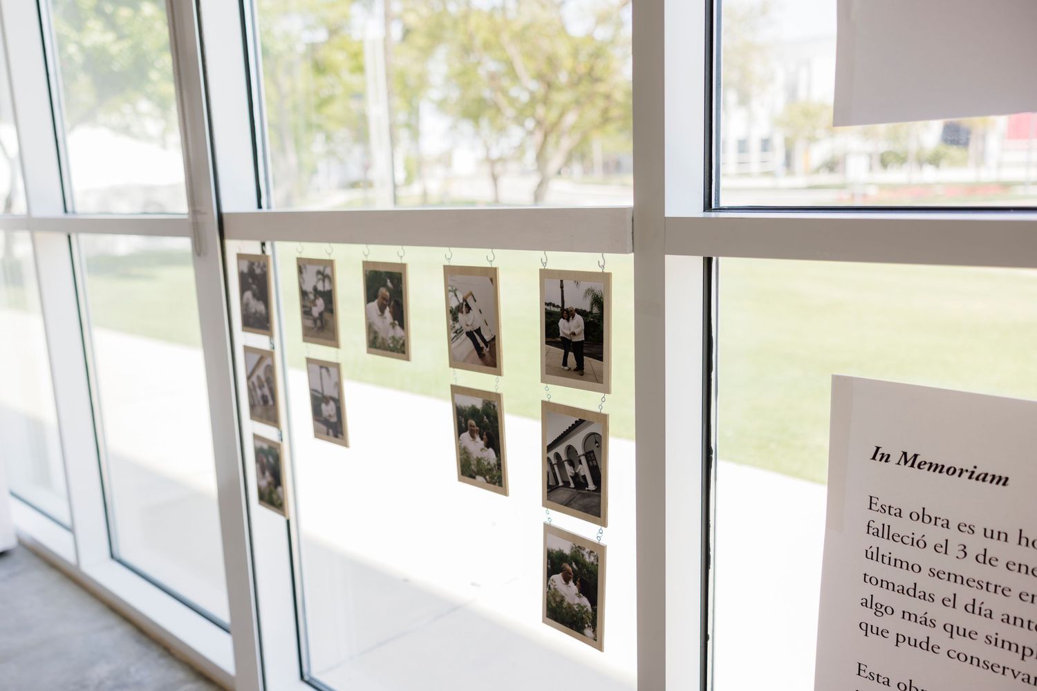 Black and white photos displayed on a glass window next to an In Memoriam plaque in a modern building.