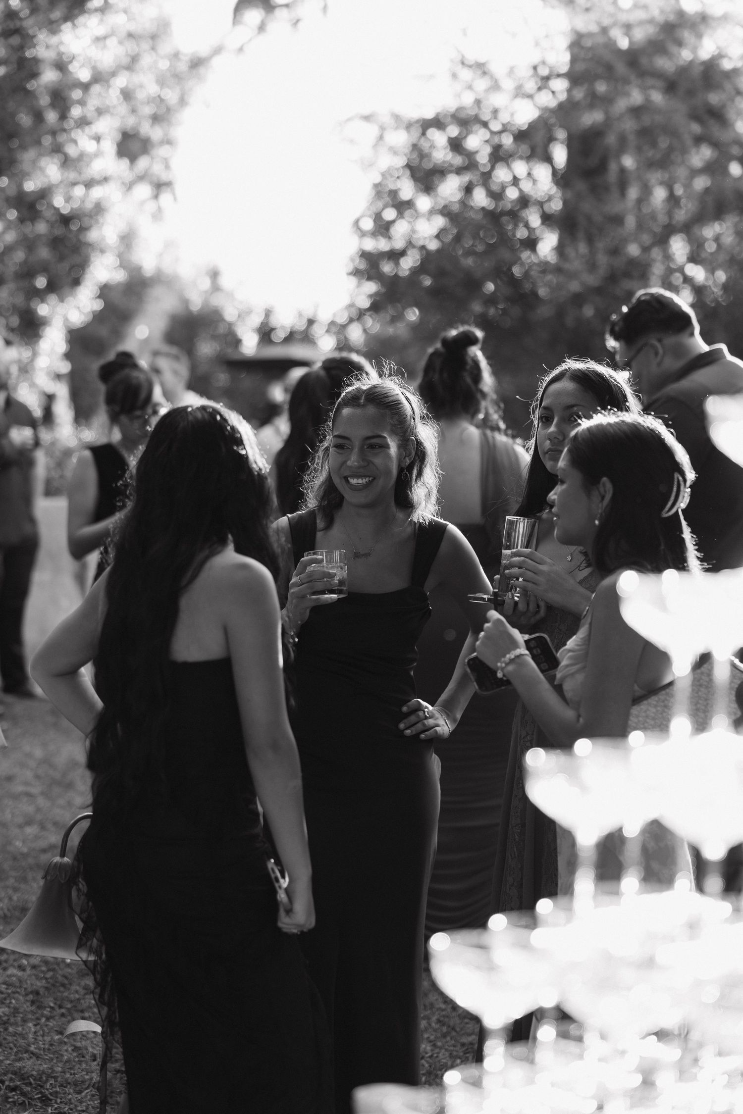 Black and white photo of guests enjoying drinks at an outdoor wedding reception.