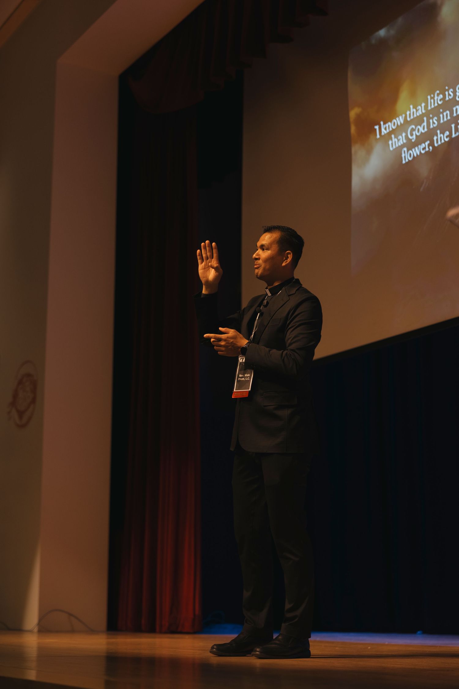 A speaker gives an animated presentation on a dark stage with projected text visible.