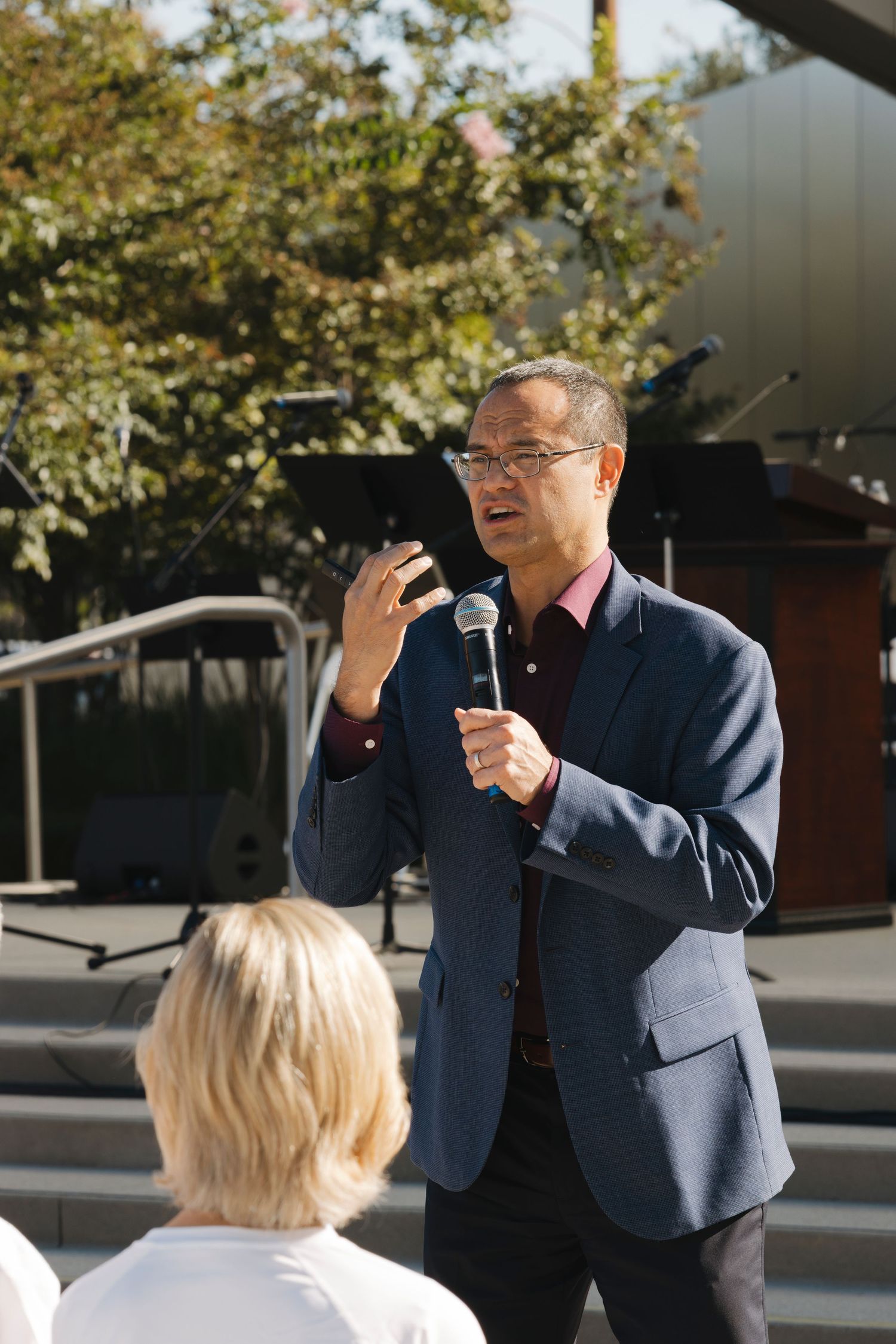 Speaker gesturing while presenting to an audience at an outdoor venue.