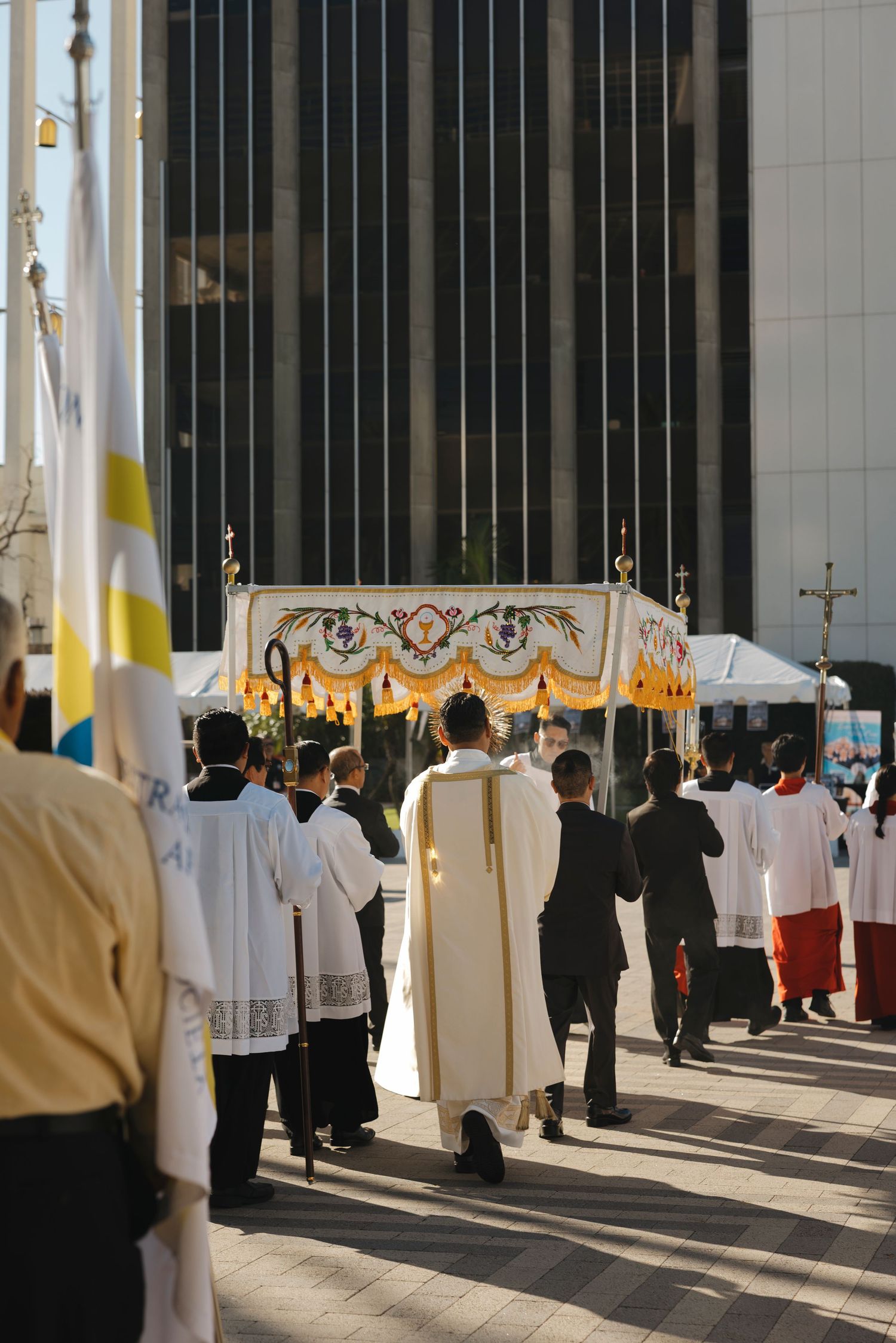 Religious procession with clergy in white robes walking through a modern church interior with columns.