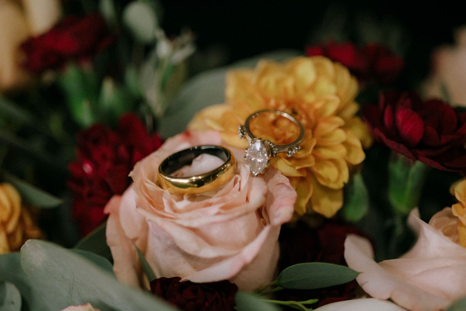 Close-up of wedding rings nestled among pink and burgundy floral arrangements.